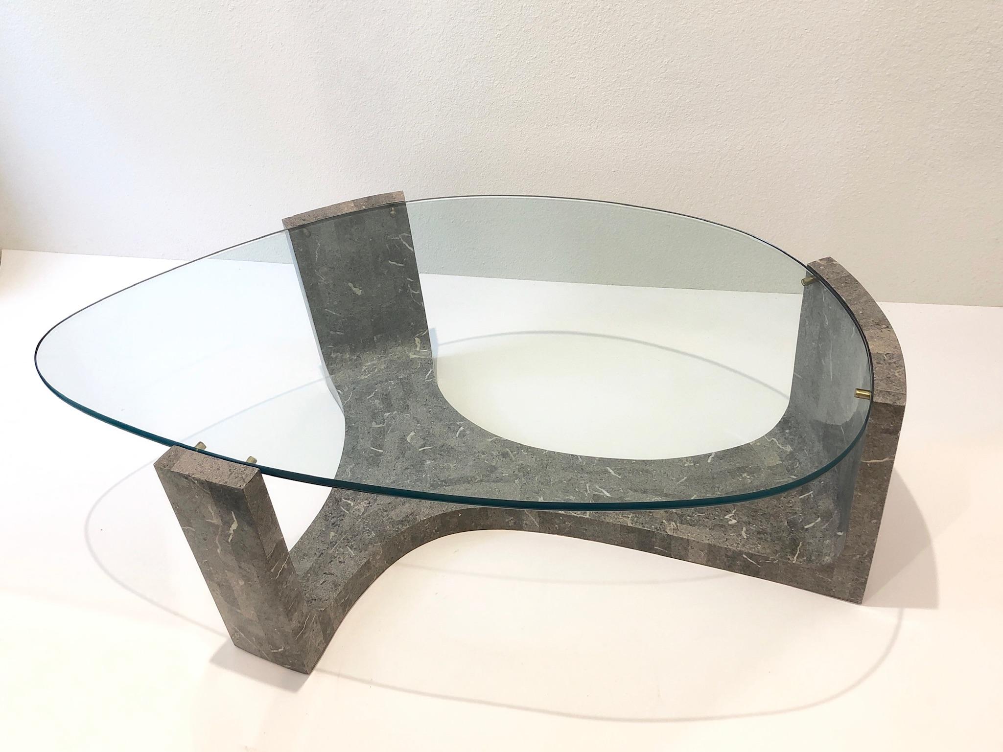 1980’s sculptural cocktail table by Maitland Smith.
Constructed of wood covered with gray tessellated marble, brass details and 5/8” thick glass top. 
Measurements: 51” Wide, 32.5” Deep and 16.25” High.
