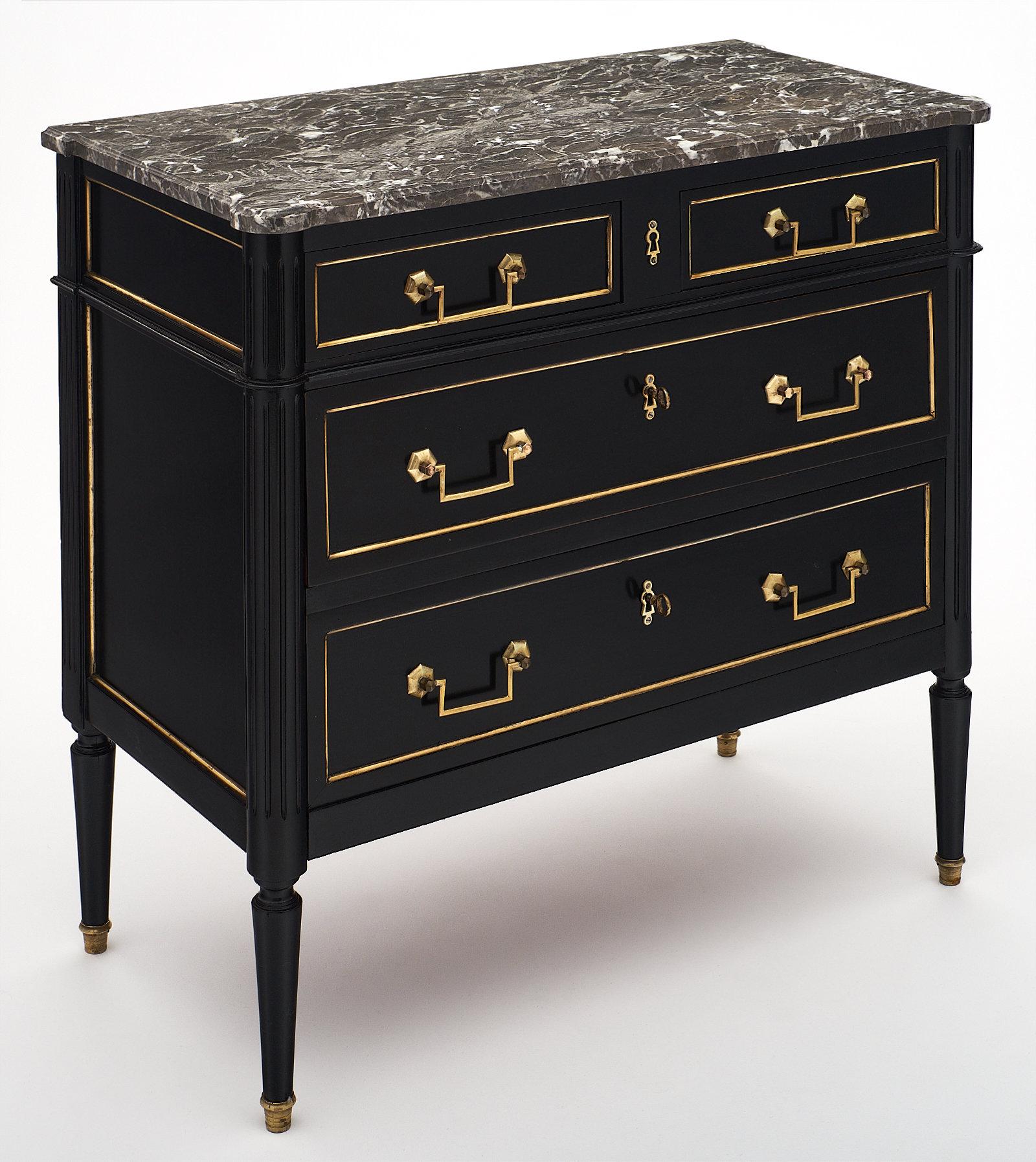 A Louis XVI style antique chest of drawers with grey marble. This piece is made of mahogany and finished with a lustrous ebonized French polish. The piece features the original gilt brass hardware with gilt trims throughout. We loved the grey veined