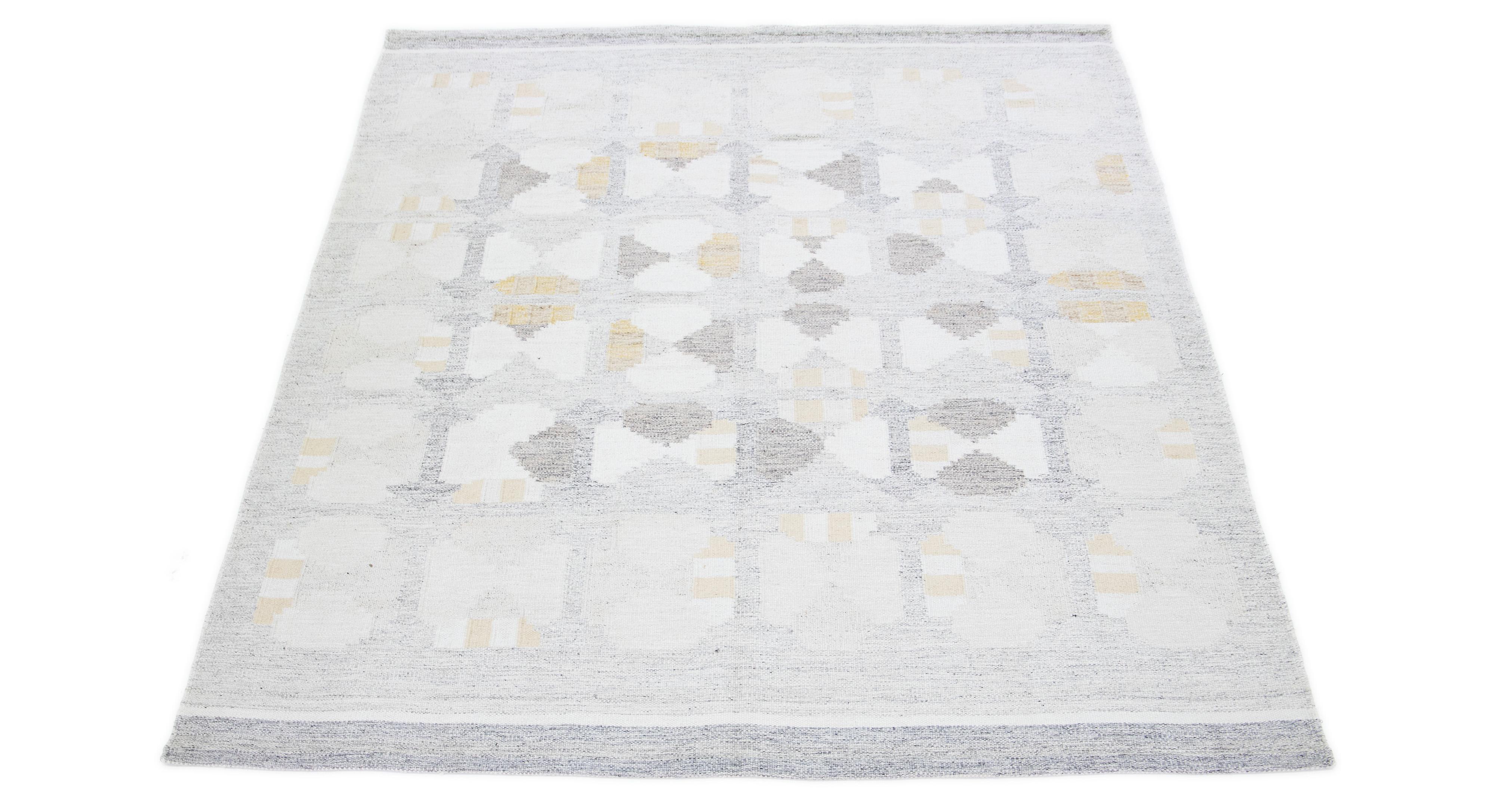The flatweave rug showcases a contemporary Swedish design with a subtle gray base. It features an elaborate geometric pattern covering the whole surface, enhanced by subdued tones of yellow and ivory.

 This rug measures 9' x 12'.


