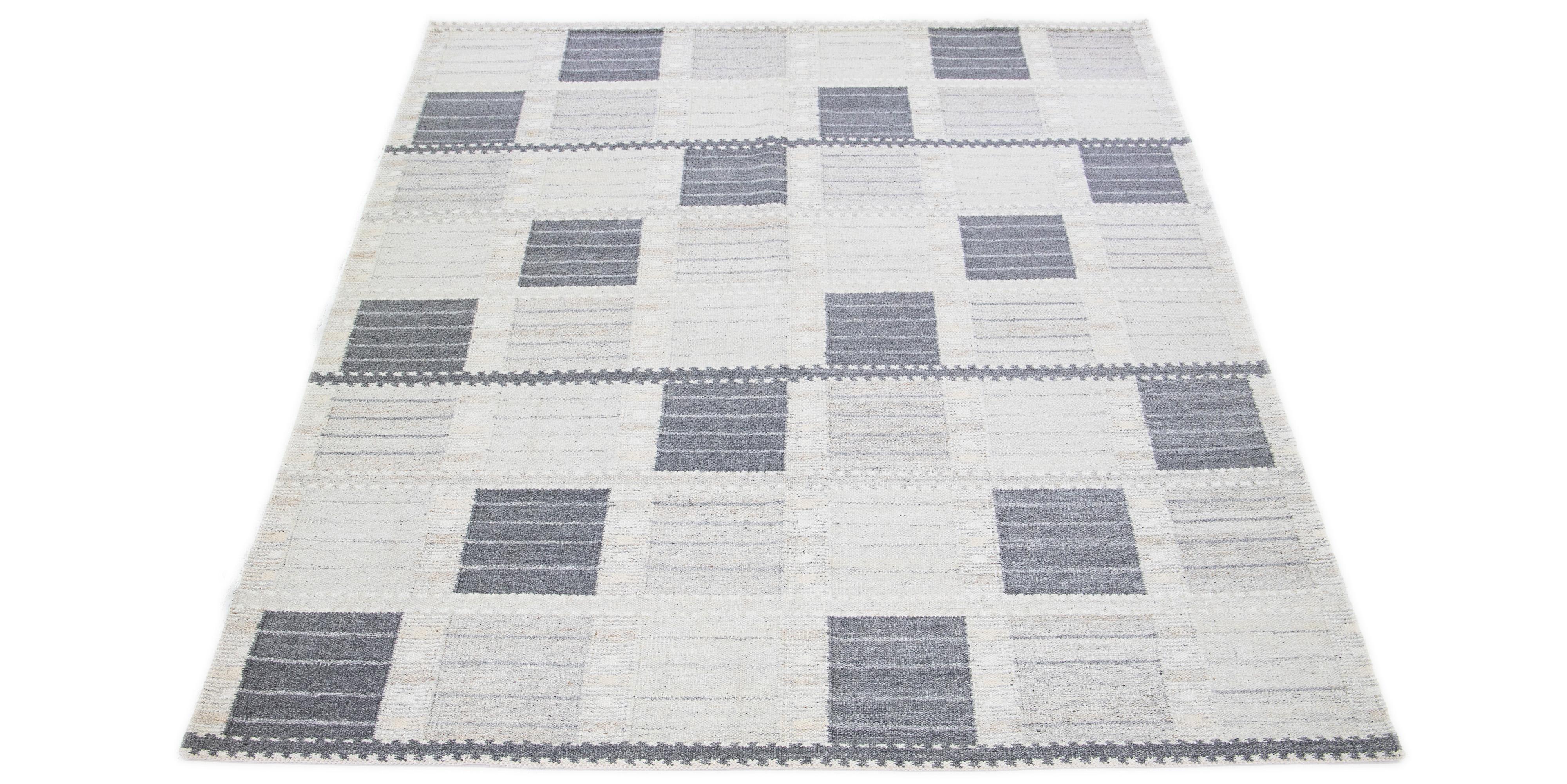 Inspired by Swedish design, this modern woolen rug features a subtle light gray backdrop. This exquisite flatweave rug is beautifully embellished with a striking geometric pattern in dark gray and beige tones.

 This rug measures 9'4
