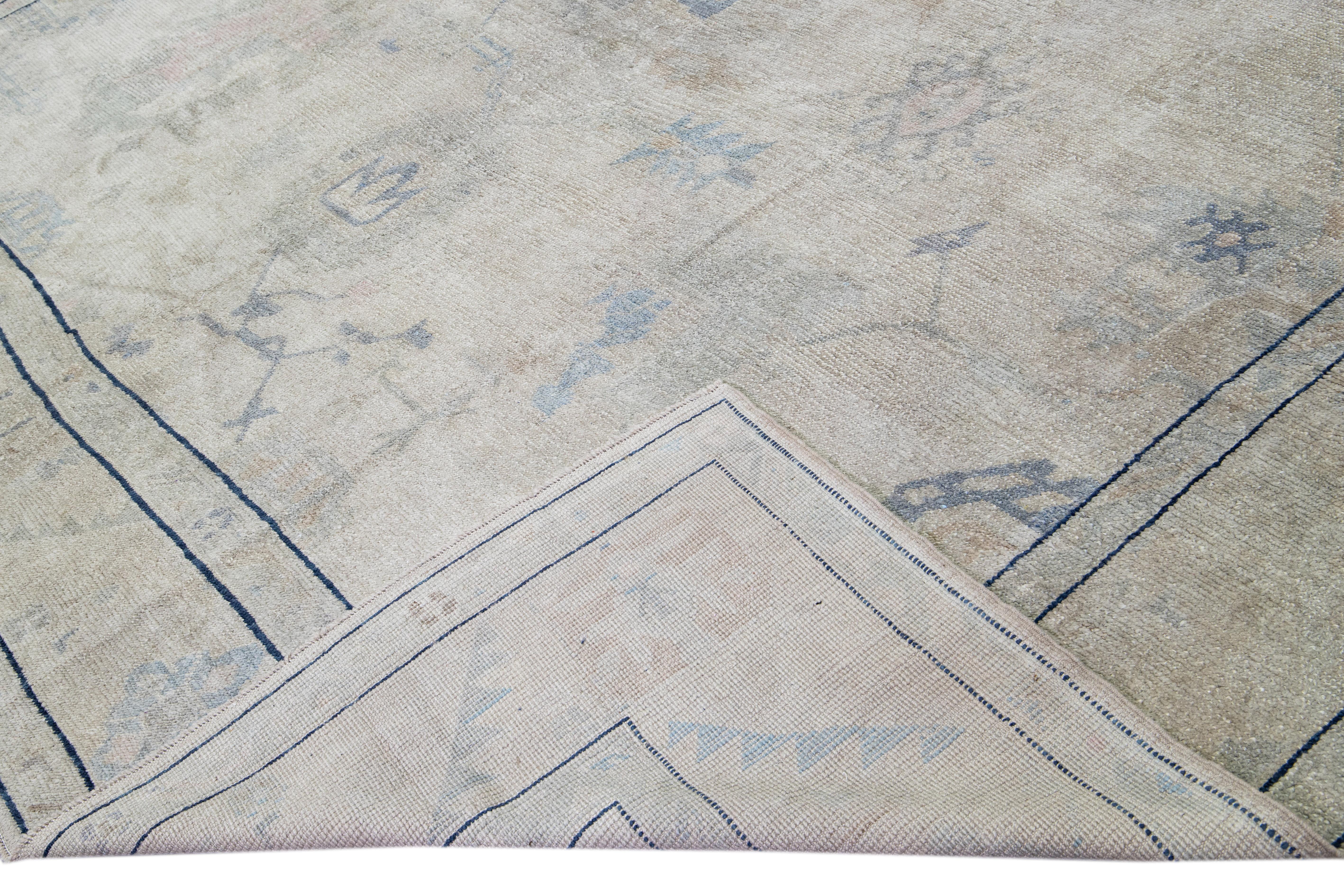 Magnifique tapis moderne Oushak en laine nouée à la main avec un champ gris. Ce tapis Oushak aux accents roses, beiges et bleus présente un magnifique motif floral géométrique. 

Ce tapis mesure : 12'4