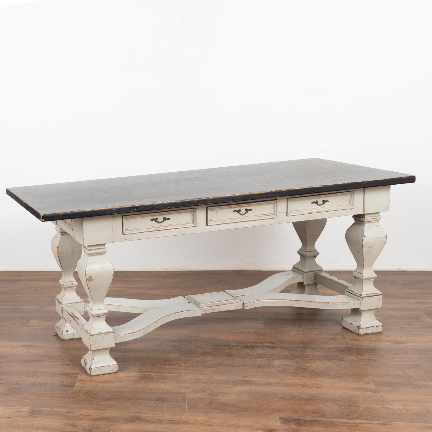 This handsome baroque pine library table with three drawers has heavily turned legs and an attractive X shaped lower stretcher.
The base has been given a newer, professionally applied layered antique gray painted finish and is lightly distressed