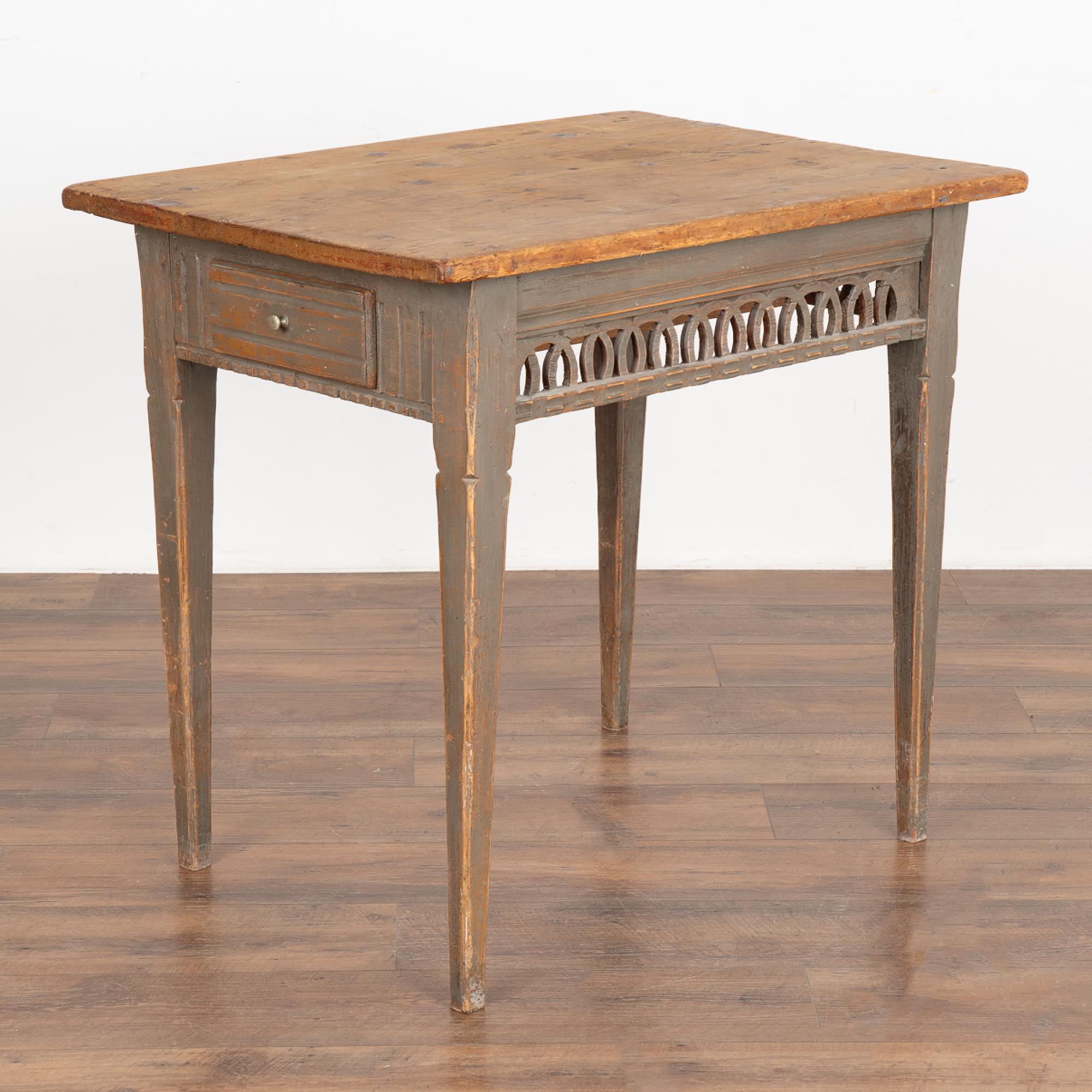 Small side table with decorative lattice work skirt and single drawer on side. 
The aged original gray painted finish is distressed through generations of use and has developed a warm and inviting patina. 
The contrasting pine top with its stains,