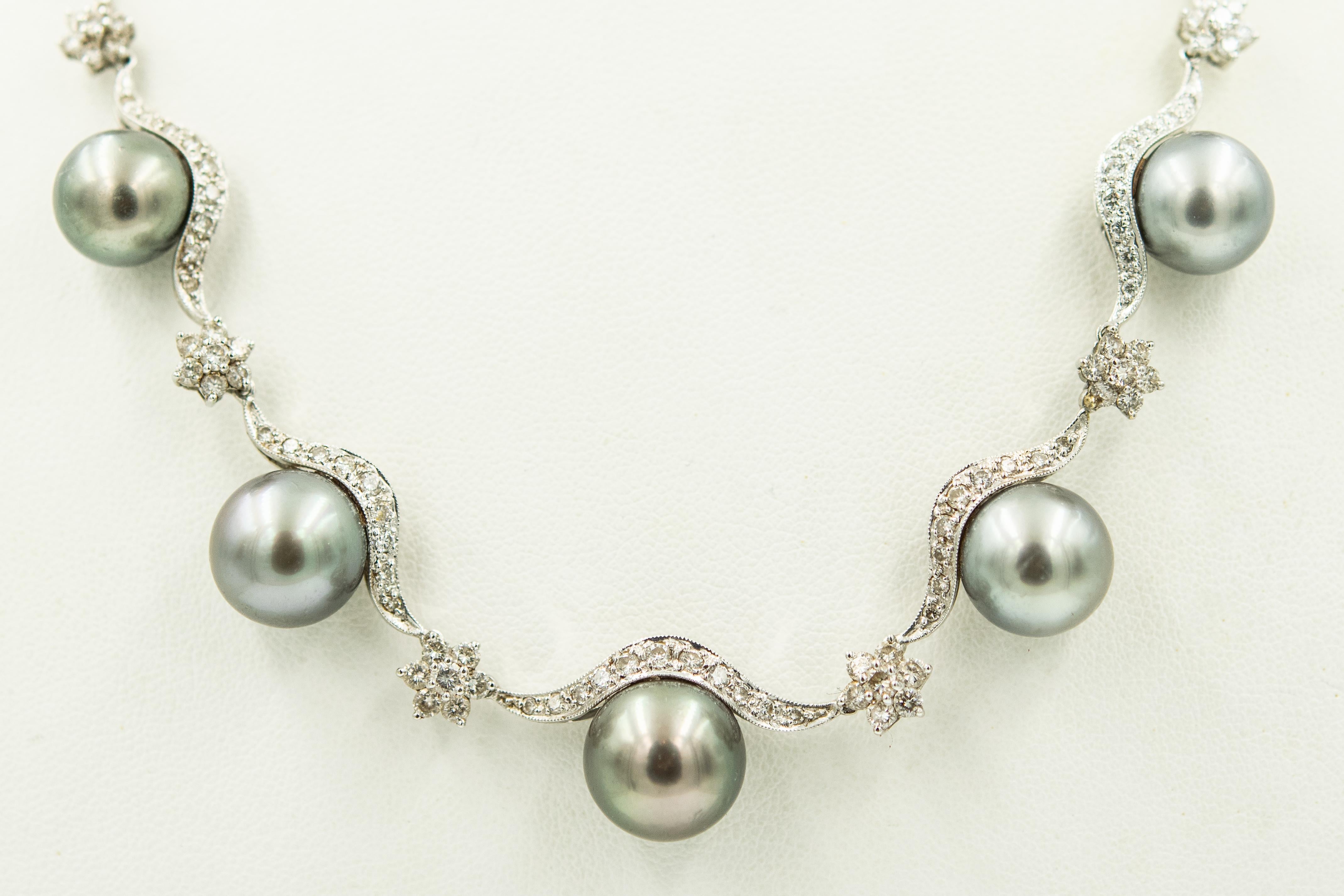 18k white gold necklace with diamond swags or scallops with diamond flower spacers and five graduating gray round cultured pearls draping across the front.  The necklace has a plunger clasp with a figure eight safety. The pearls measure