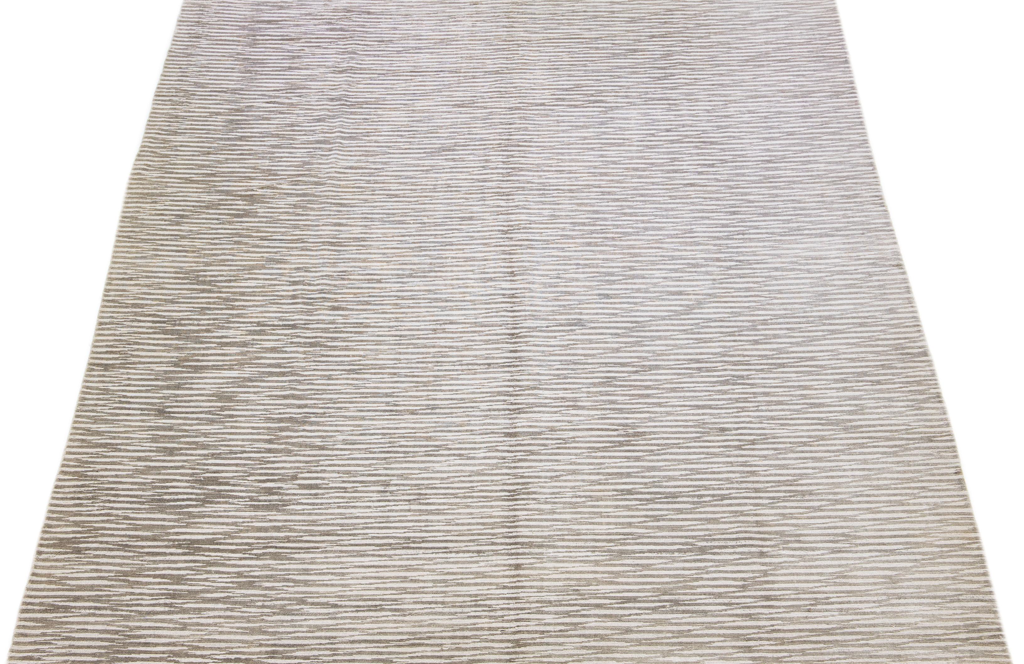 Dieser exquisite zeitgenössische Teppich aus Wolle und Seide hat einen auffälligen grauen Untergrund, der mit einem atemberaubenden geometrischen Muster verziert ist, das anmutig von einem Ende zum anderen fließt.

Dieser Teppich misst 9'11