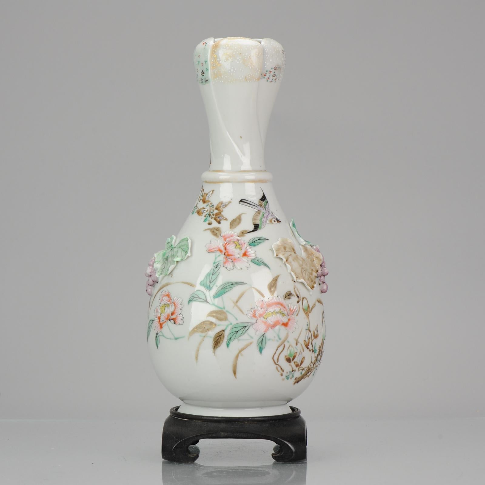 A Japanese porcelain vase, unusual in shape and with beautiful relief application of grapes and leaves. Painted scene all over of flowers and a bird in flight.
Swirled top in the shape of a flower.
Stand is included.

Condition
/ Overall