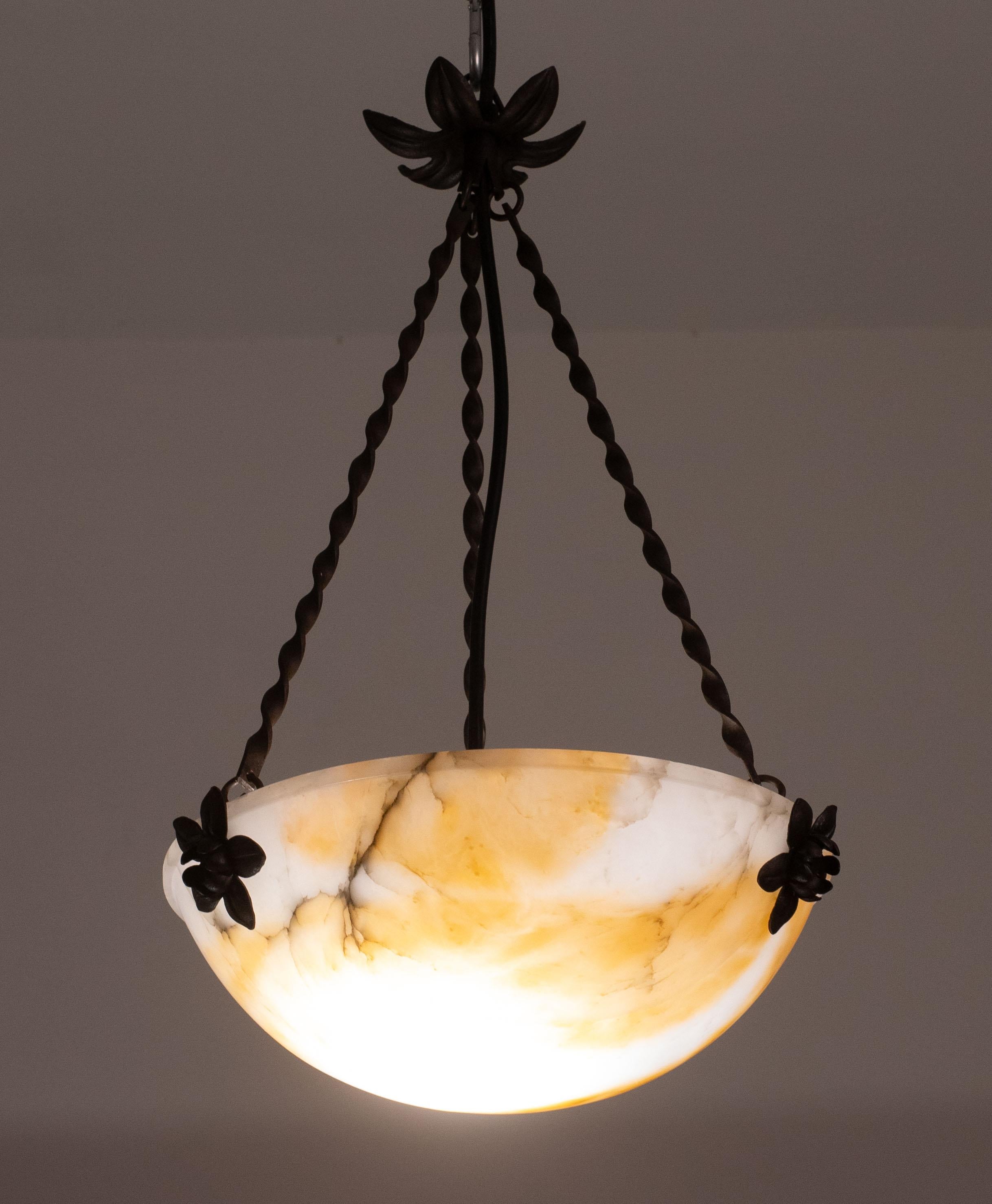 Lampada a sospensione antica in alabastro in stile Art Déco, anni '1950 circa.
Un unico pezzo di alabastro, splendidamente lavorato con sfumature e riflessi di altri colori quando viene illuminato, sospeso a tre catene di ferro battuto nero