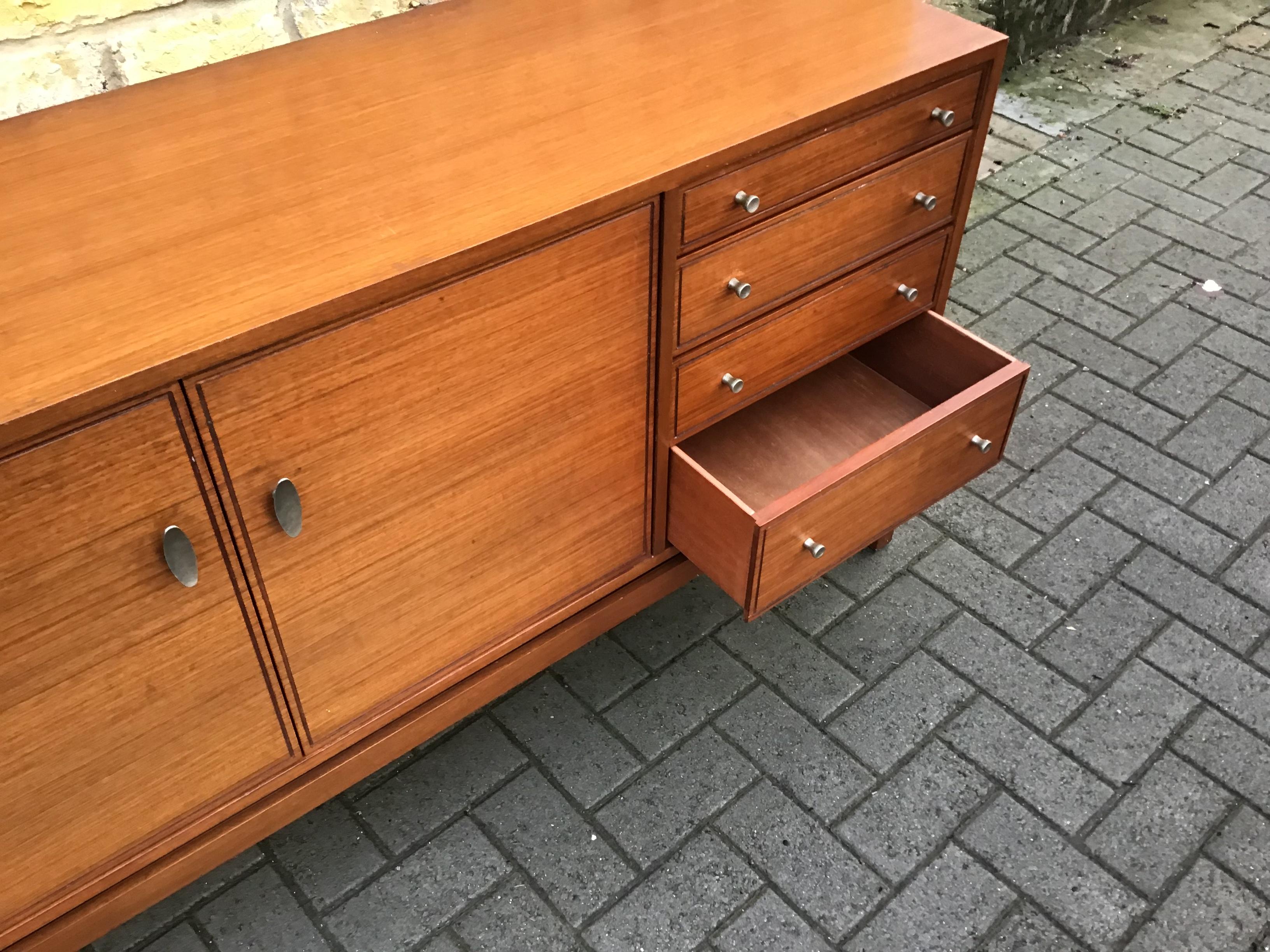 A small and perfectly formed midcentury teak sideboard. It has a double cupboard with an internal shelf and space for bottles and 4 drawers, the top one divided and lined for cutlery, circa 1960s Greaves & Thomas.