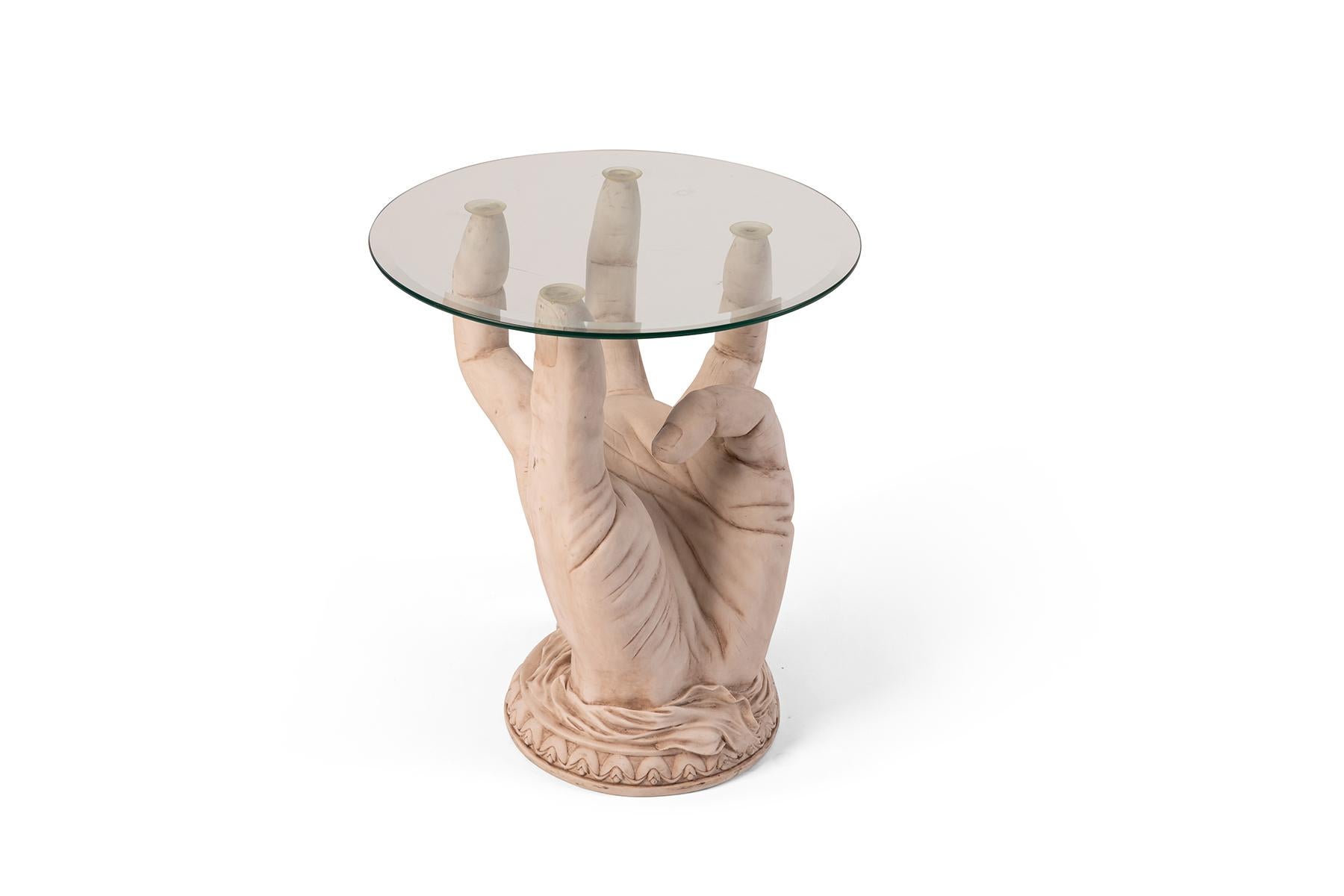 A hand sculpted from resin creates a memorable side table with a circular glass top, circa early 1970s.
