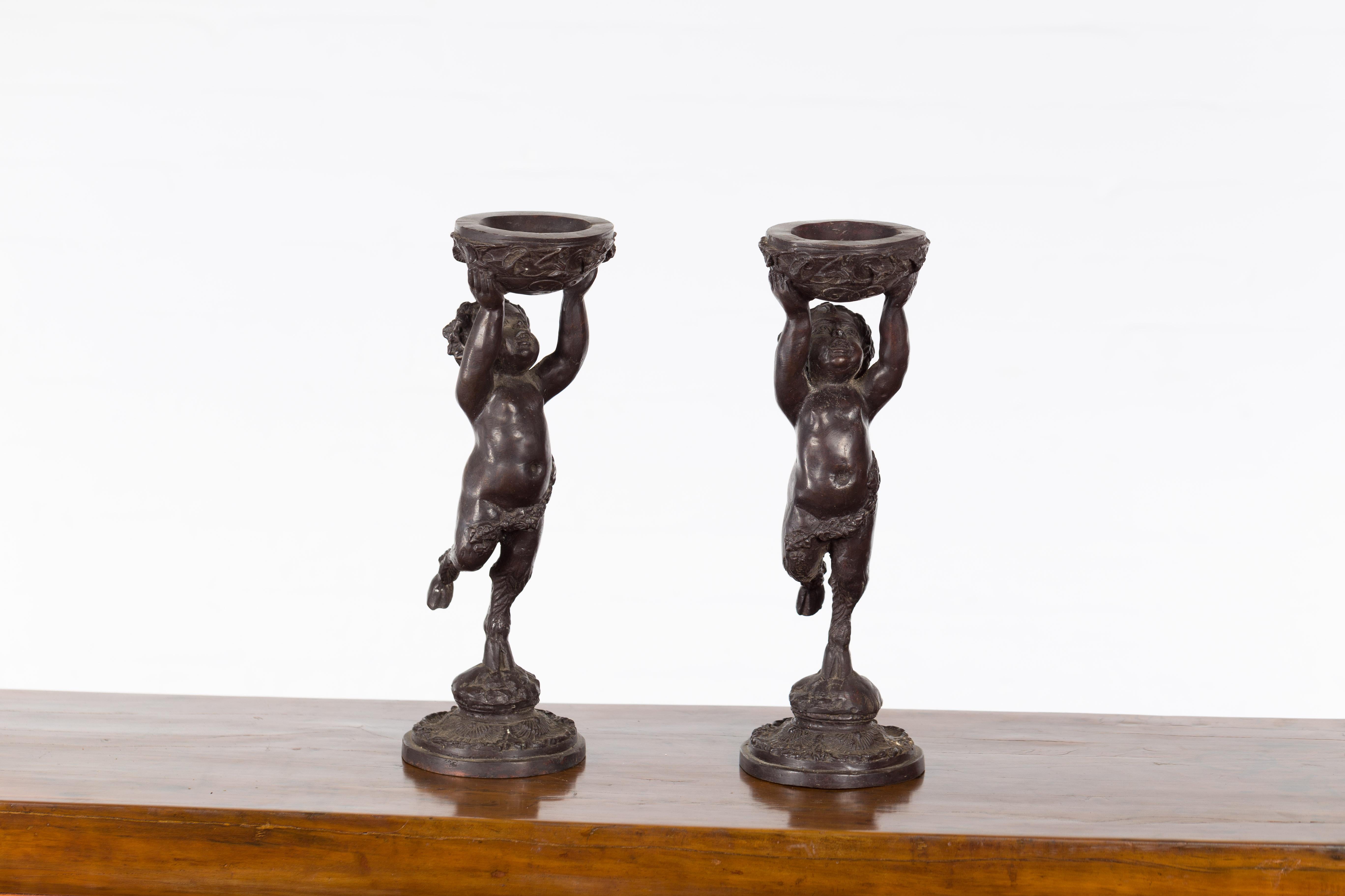 Cast Greco-Roman Style Bronze Candle Holders Depicting Young Satyrs Holding Vessels For Sale