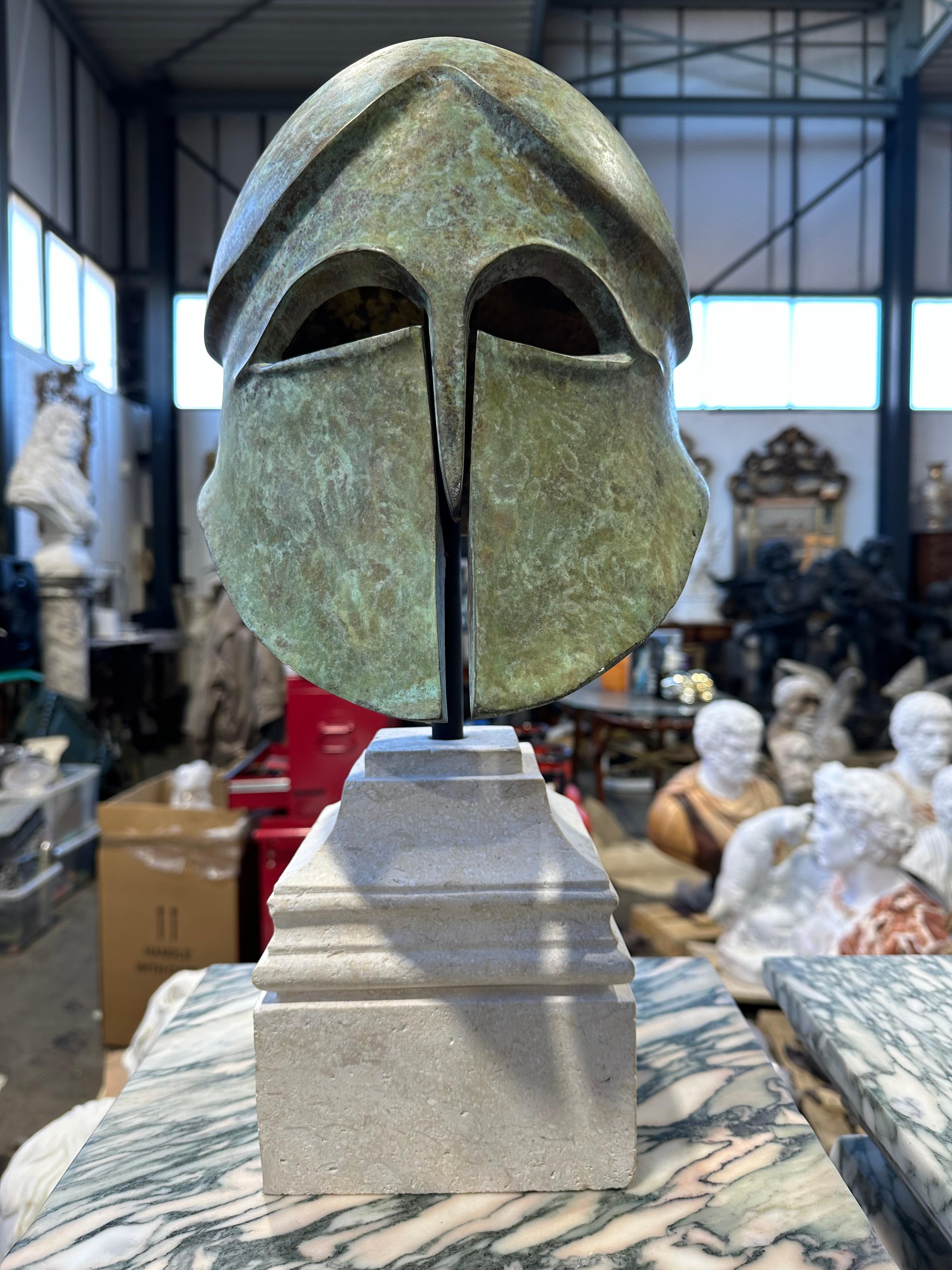 A Classical Greek Corinthian style warriors helmet in bronze on a limestone base. Reminiscent of ancient Greek warriors this helmet has a wonderful green verdigris patina and has a good weight to it. A stylish piece that would look stunning as a
