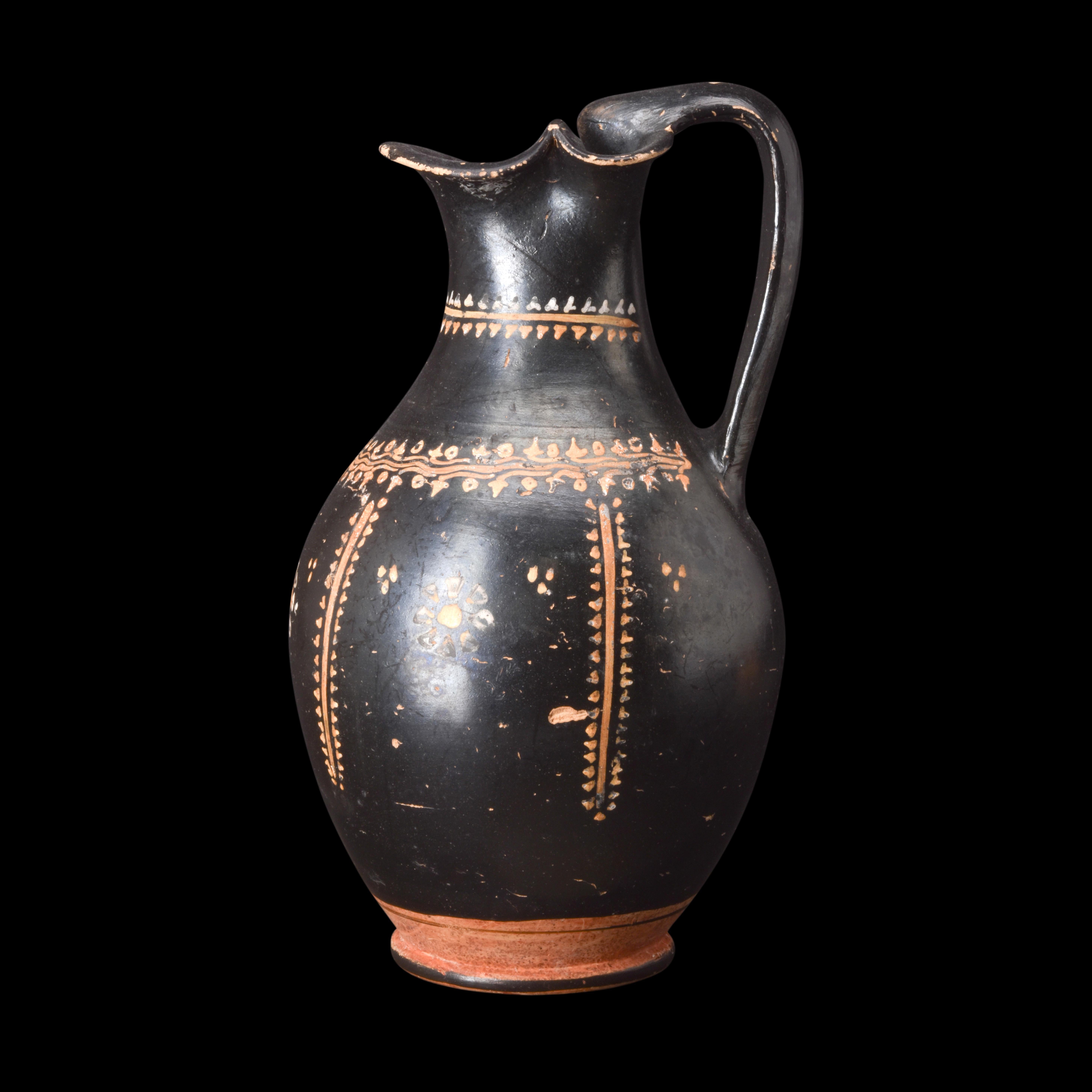 Eine schwarz glasierte Oinochoe, die die charakteristischen Merkmale dieser speziellen griechischen Keramik aufweist. Das Gefäß hat einen abgerundeten Körper mit einer zarten Riffelung, die sich zum Fuß hin anmutig verjüngt. Der Hals des Gefäßes