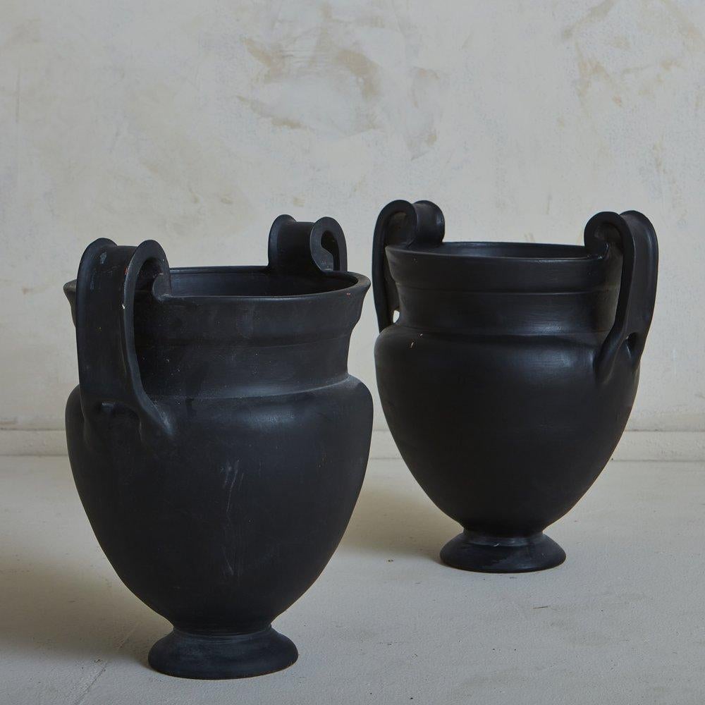 20th Century Greek black terra cotta urns have curved handles and circular pedestal bases. 1 Available; Priced Individually.