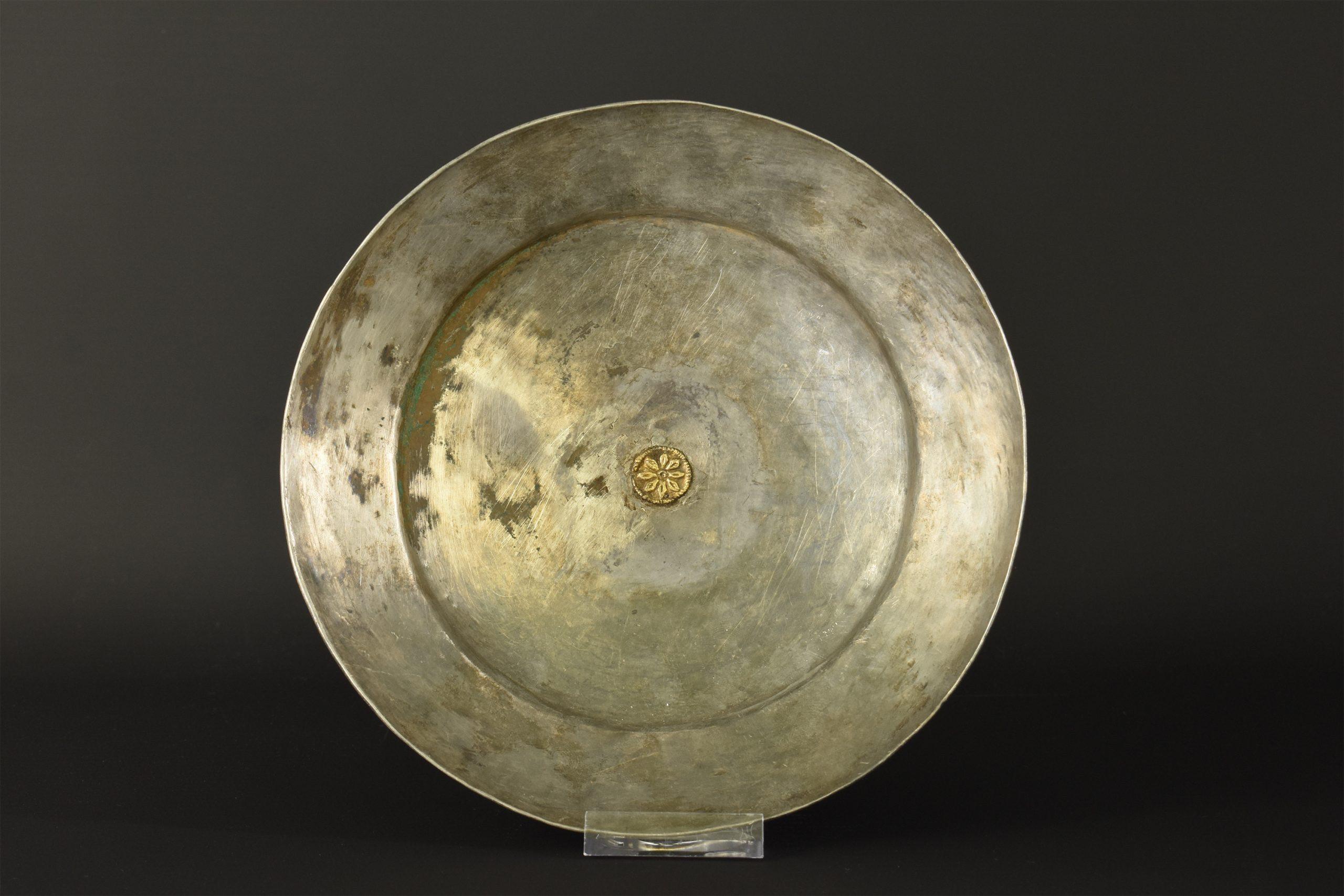 A fantastic phiale formed by a single hammered silver sheet; a smooth surface with a slightly flanged, corseted neck, a flared, unpronounced rim and a shallow interior, circa 400-300 BC. The central part is decorated with an applied gilded rosette.