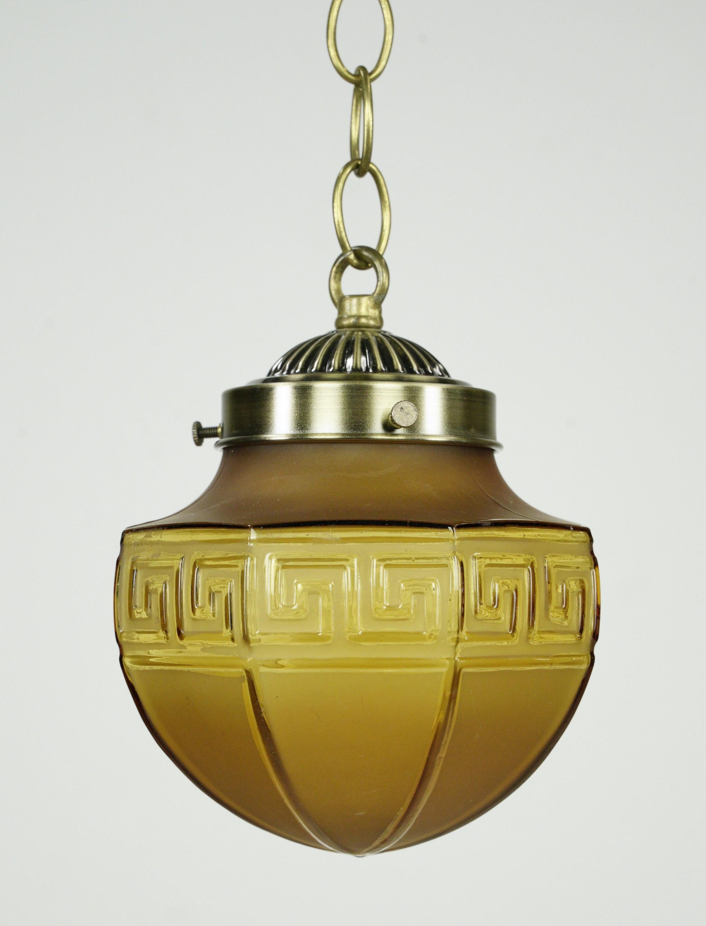 Lampe suspendue en verre ambré avec un design en forme de clé grecque et une quincaillerie en acier plaqué laiton. Elle nécessite une ampoule standard à culot moyen. Le prix comprend la restauration, le nettoyage et le recâblage. Un disponible.