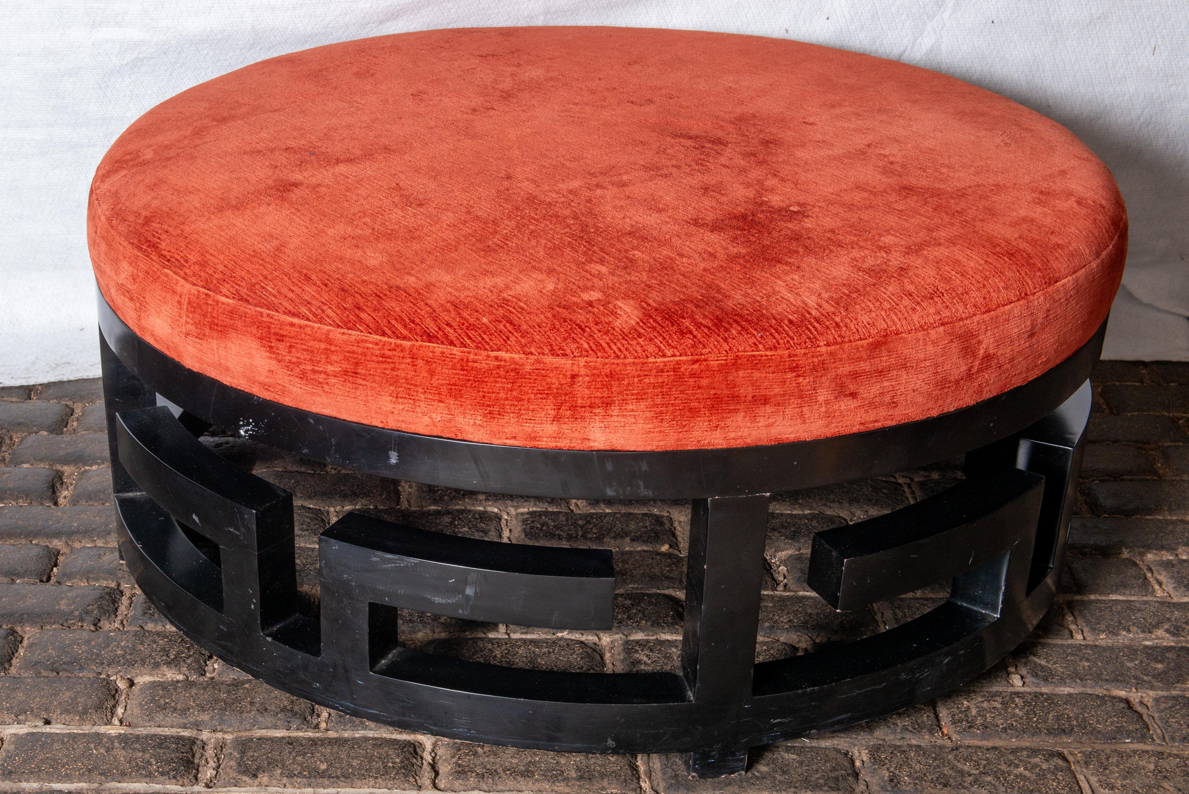 This is a very unusual, highly dramatic huge round ottoman, bourne, or round sofa.  The curved, dark stained wood base features a giant sized carved three dimensional Greek Key design. Orange-red velvet is in very good condition. This piece would be