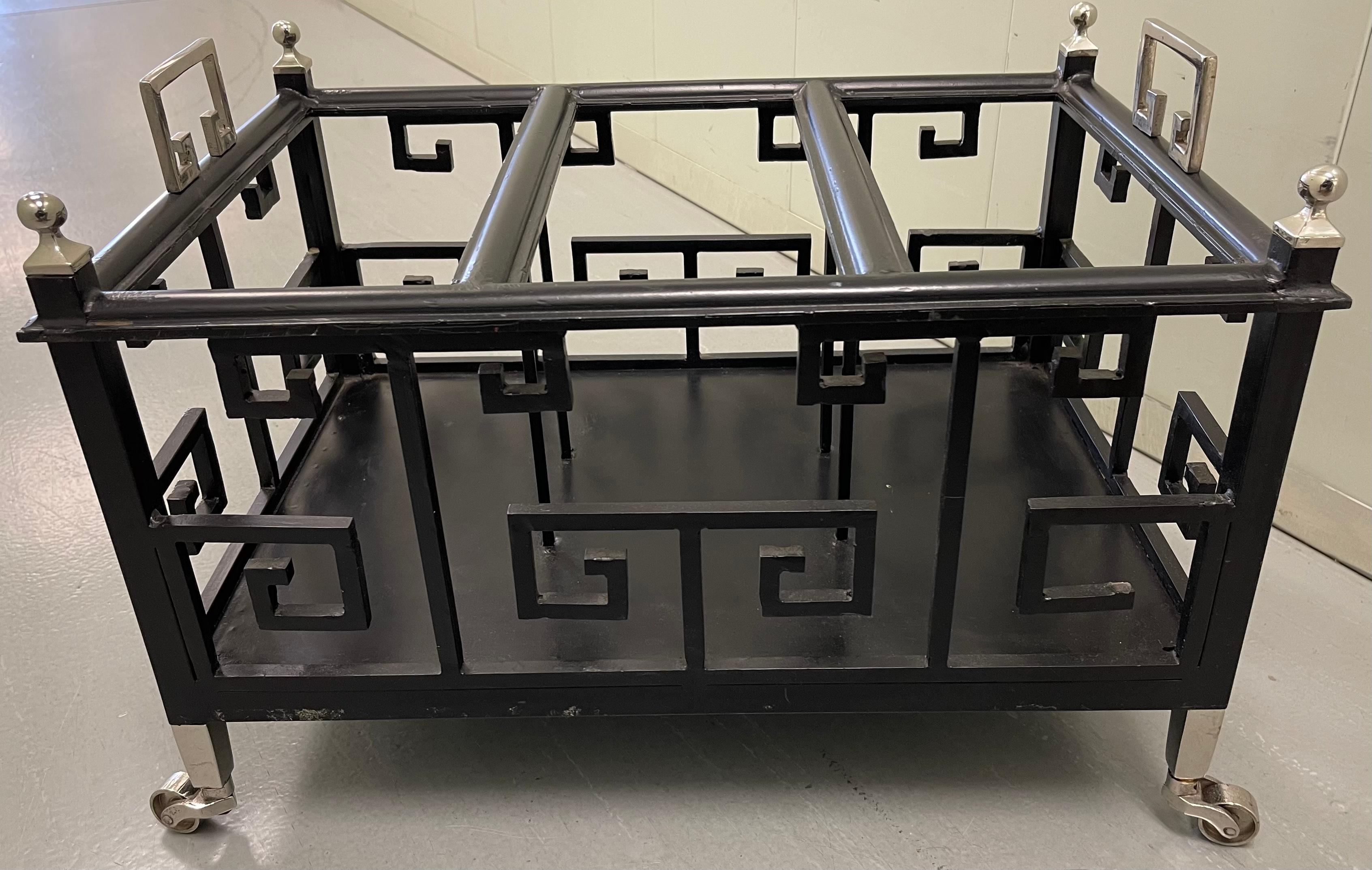 Black wrought iron Greek key motif Canterbury or magazine rack. Polished nickel handles and ball finals. Polished nickel wheels are in working condition. No makers mark or signature. Very well made, heavy piece.