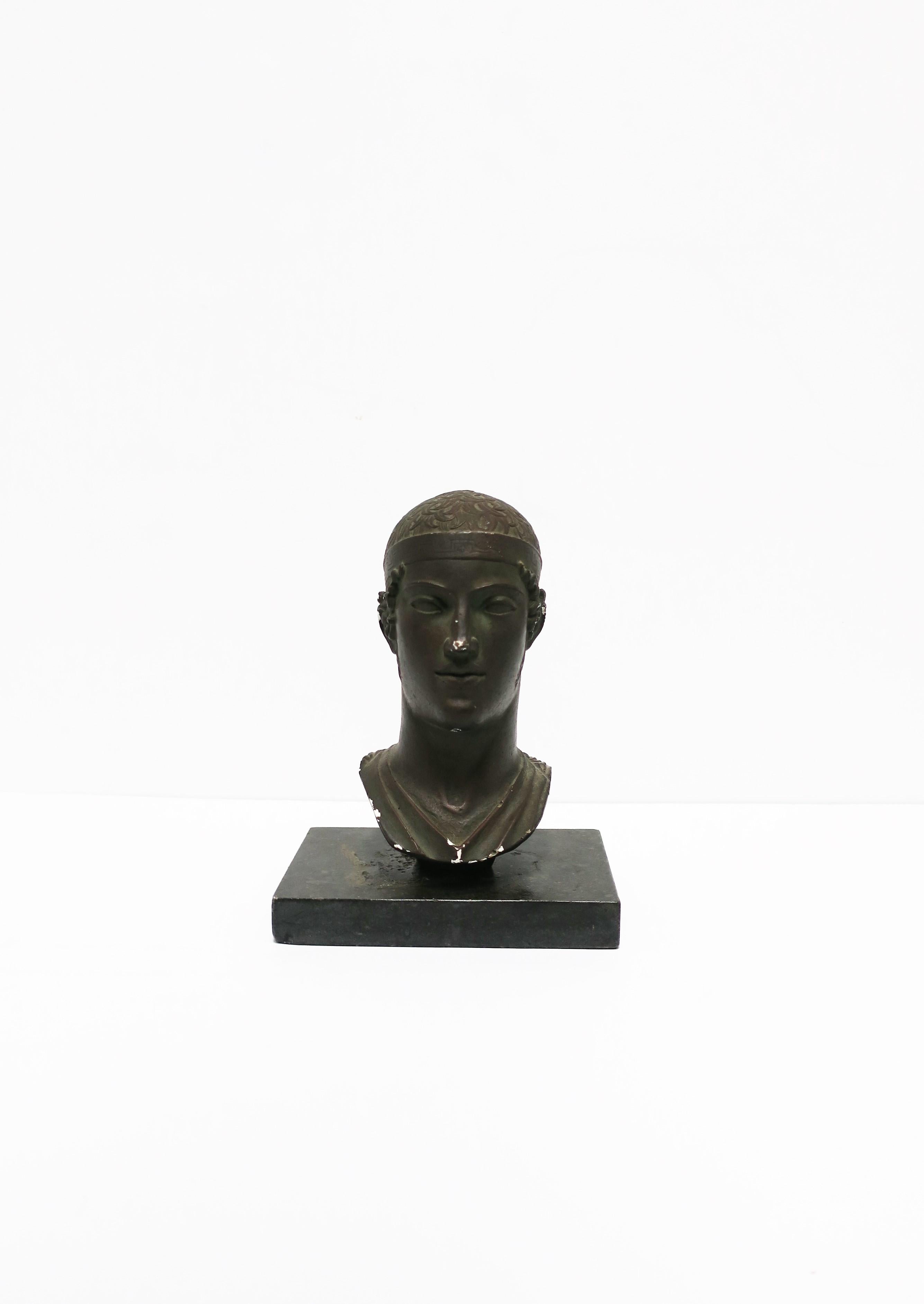 A Greco-Roman sculpture head or bust, England, 1965. A reproduction piece made of chalkware or plaster with a dark bronze-like finish. Marked on side as show in image #17. Vintage stone plinth base also included.

Sculpture measures: 8.25