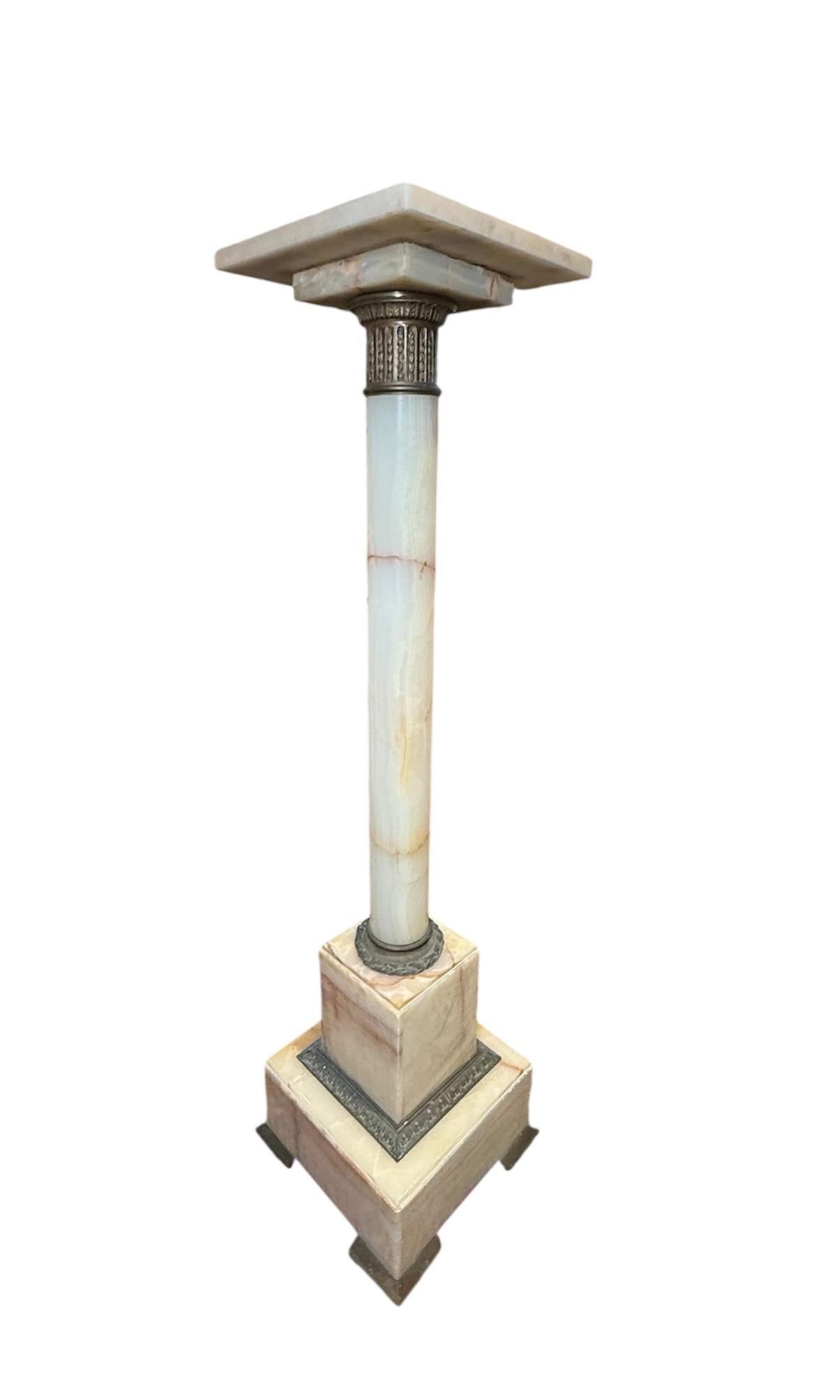Si tratta di un piedistallo in bronzo alabastro di epoca greca. Raffigura una colonna dorica in alabastro perlato decorata con bande di bronzo patinato nella parte superiore e inferiore. L'ampia fascia superiore in bronzo è ornata da un motivo a