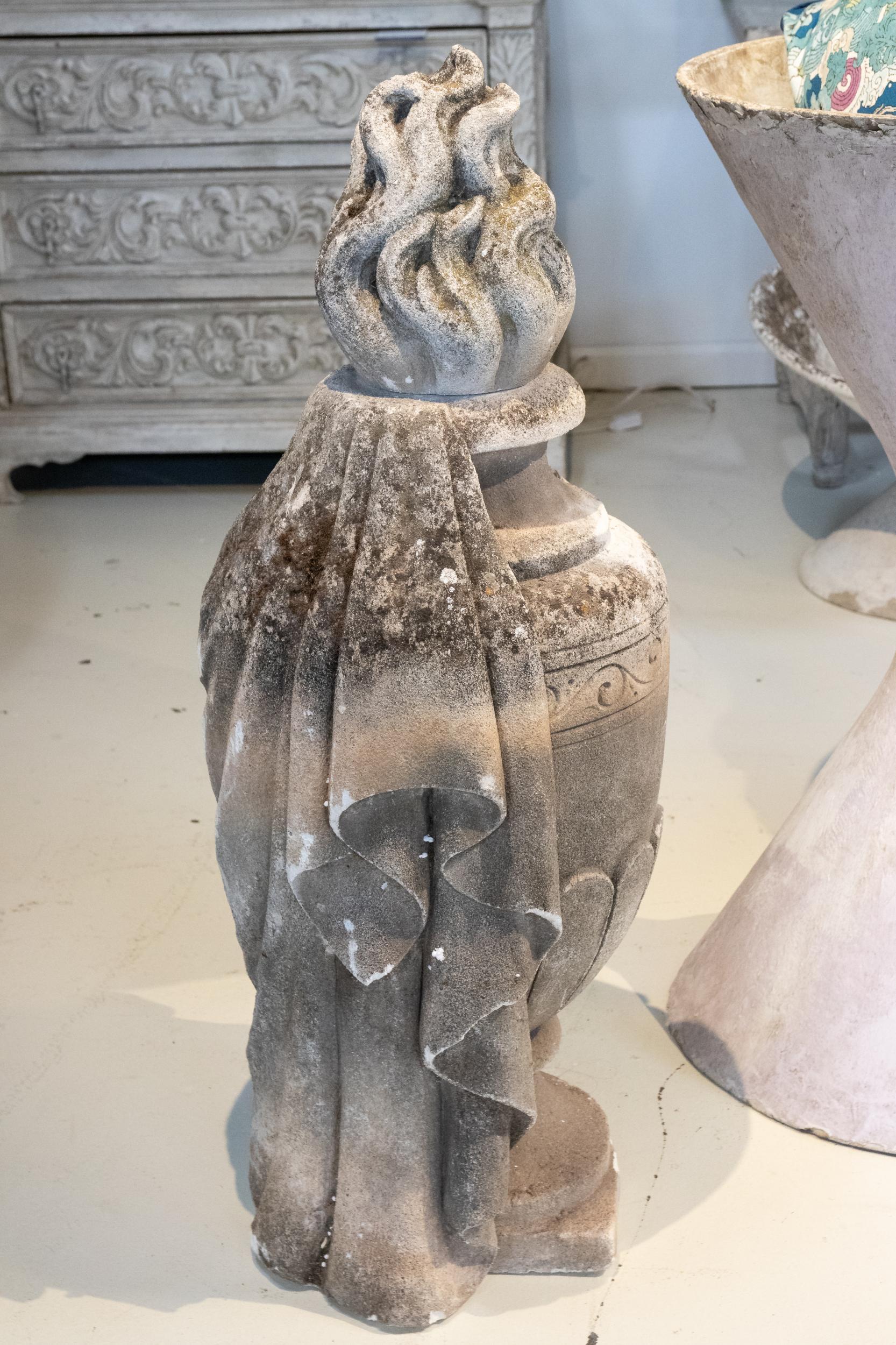 Early 20th century Grecian style draped cast stone urn with a flame shaped finial and scrollwork trim on the body. Please note of wear consistent with age including weathered finish and damage on one corner of the square plinth base.