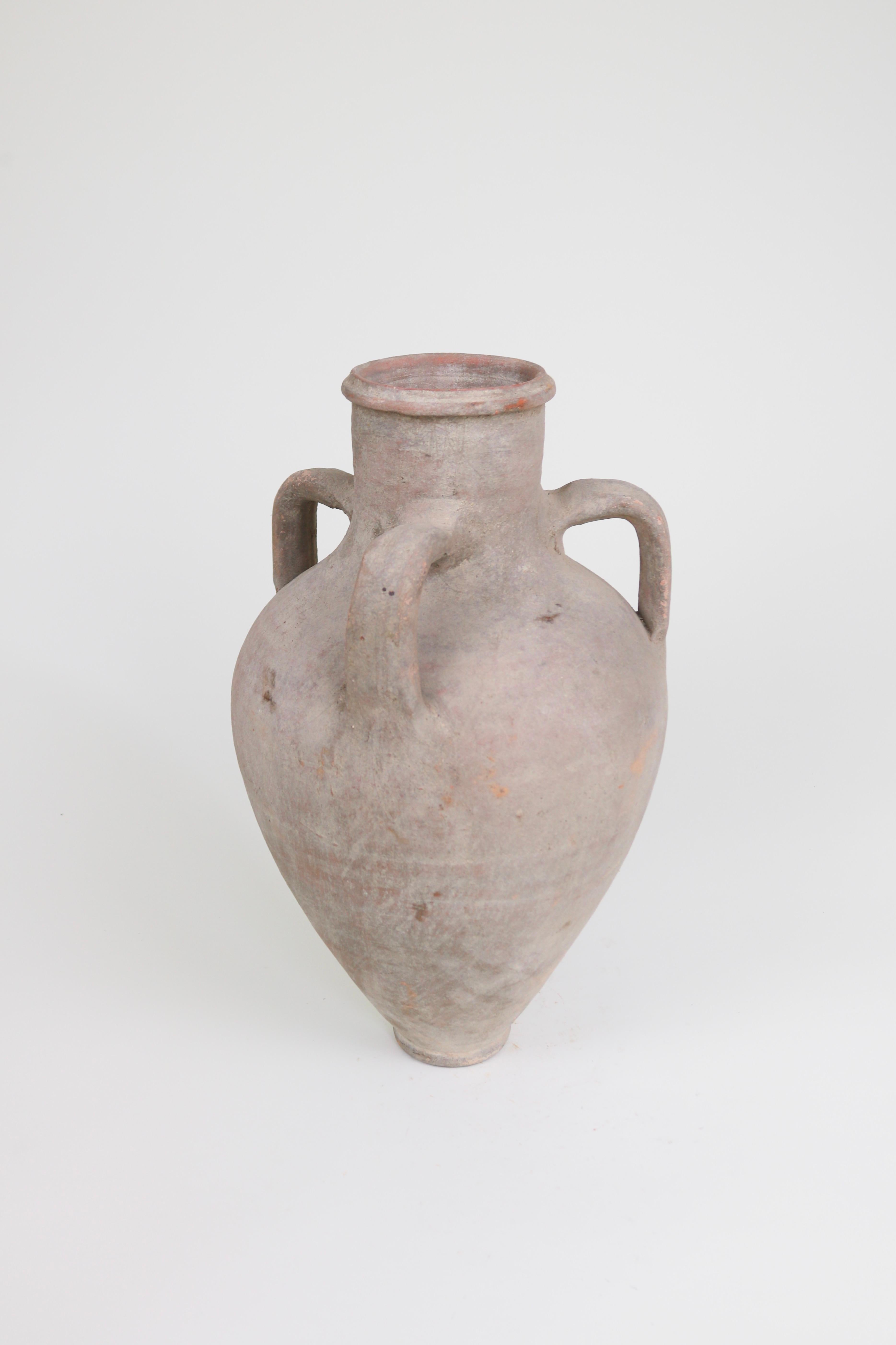 Diese dreiarmige griechische Amphora wurde Anfang des 20. Jahrhunderts zur Aufbewahrung und zum Transport von Flüssigkeiten verwendet. Mit ihrer elegant verjüngten Form und den ungewöhnlichen drei Armen ist diese staubfarbene Amphora ein schönes