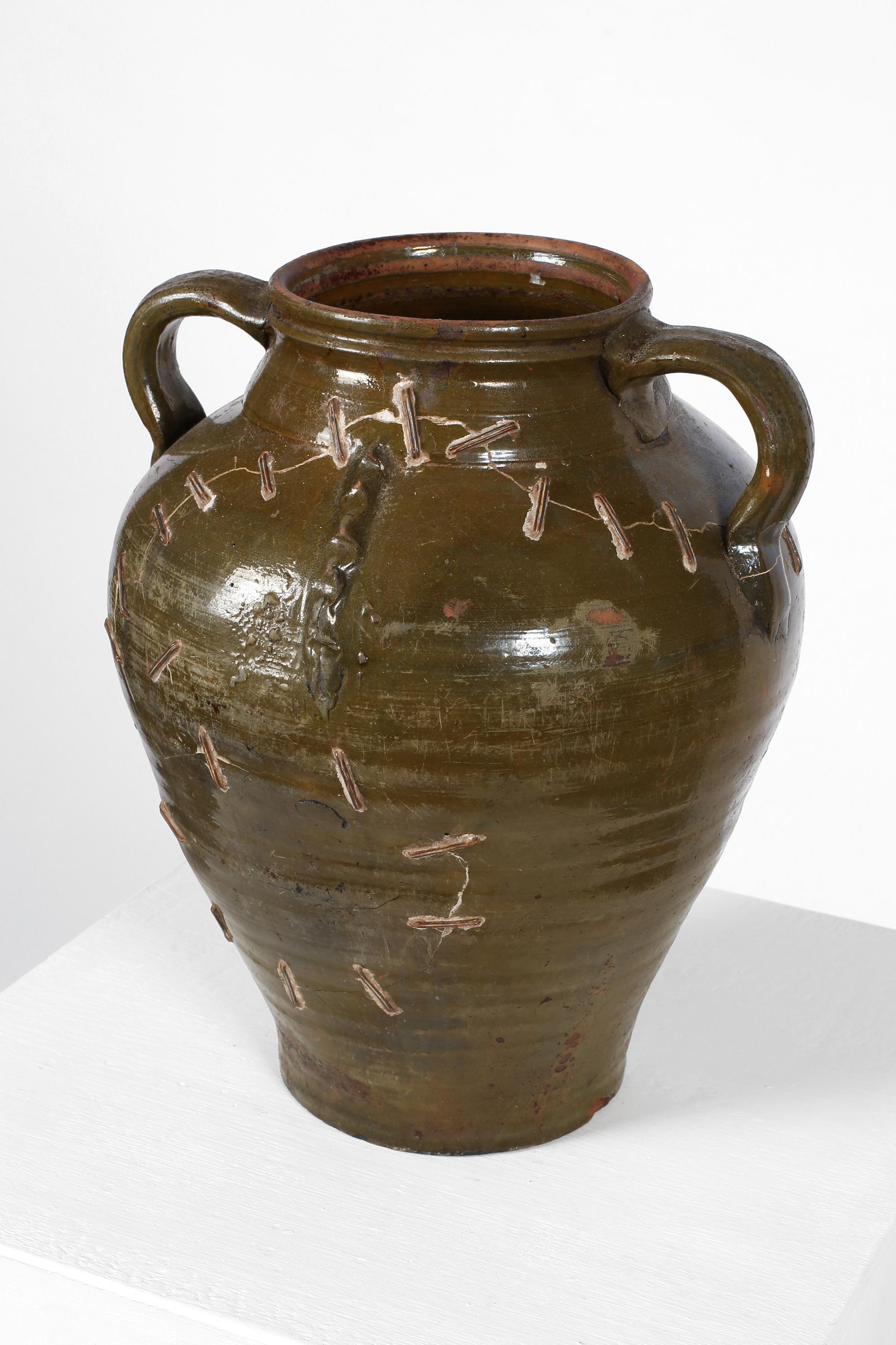 A 19th century dark olive green glazed earthenware jar from Andalusia with twin handles and characterful iron staple repairs. Spanish, c. 1850.