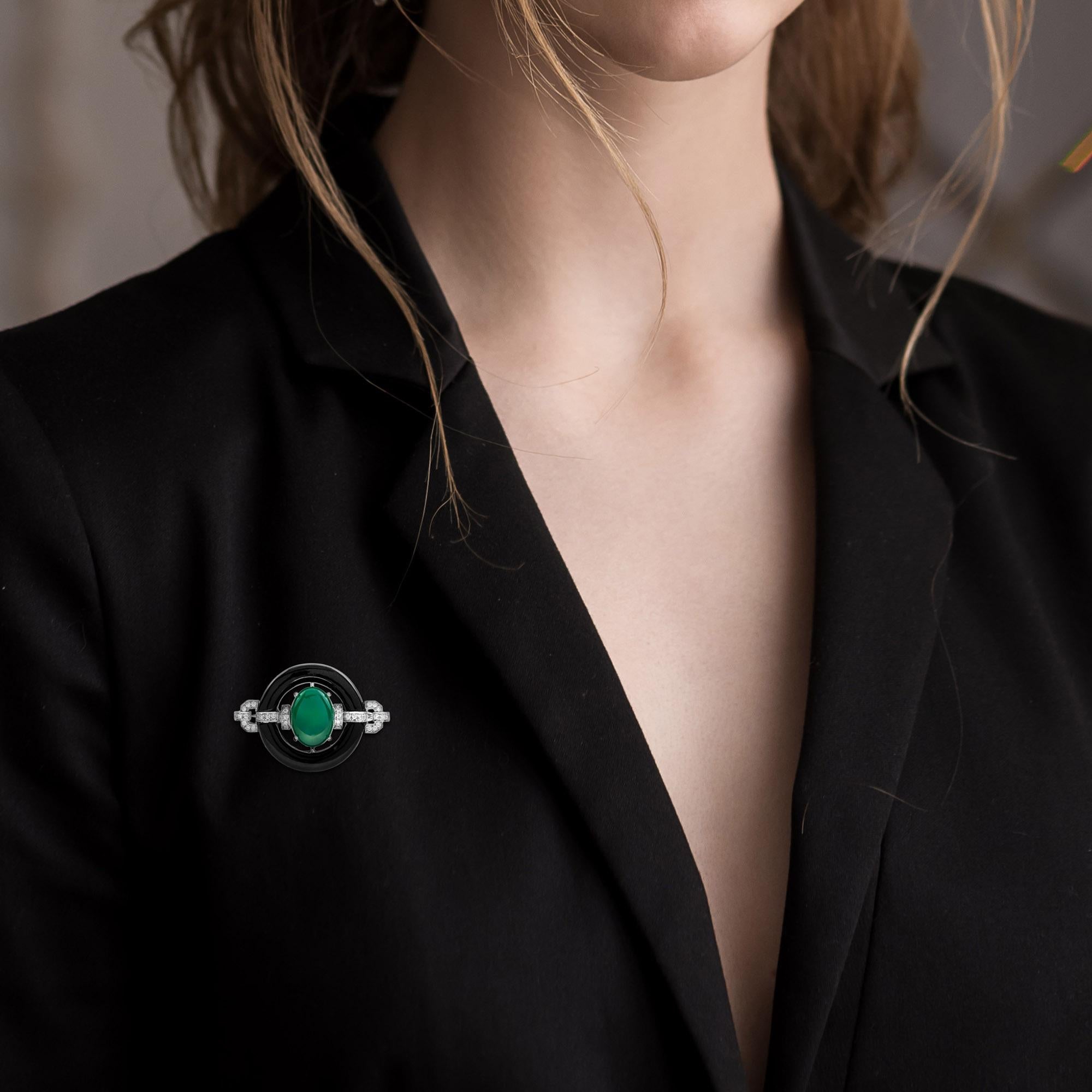 Striking, to state the obvious, this Art Deco inspired brooch, centering a 5 carat cabochon  green agate. A surrounding black donut or ‘bi’ in Chinese is grasped on either end by beautiful glittering diamonds. Crafted in white gold, this subtle