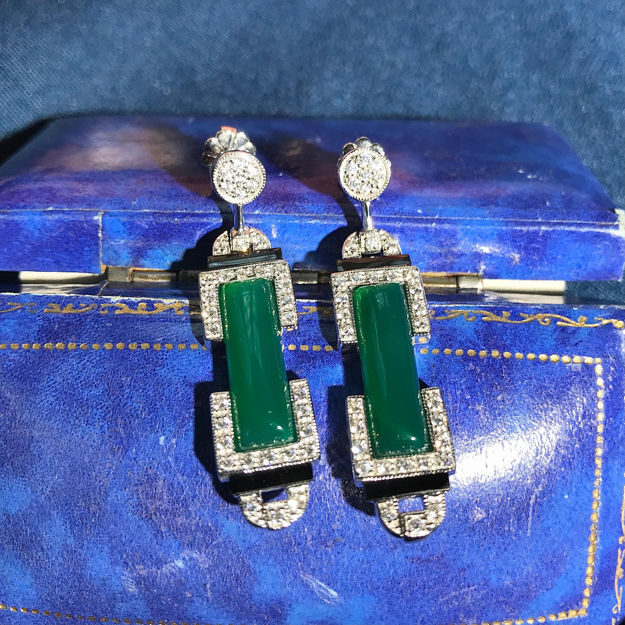 These eye-catching long, dangle-style earrings are made from white gold and feature beautiful green agate stone. The agate is carved into modern, long bars decorate glittering diamonds and onyx at the top and bottom. Hanging from circular-shaped