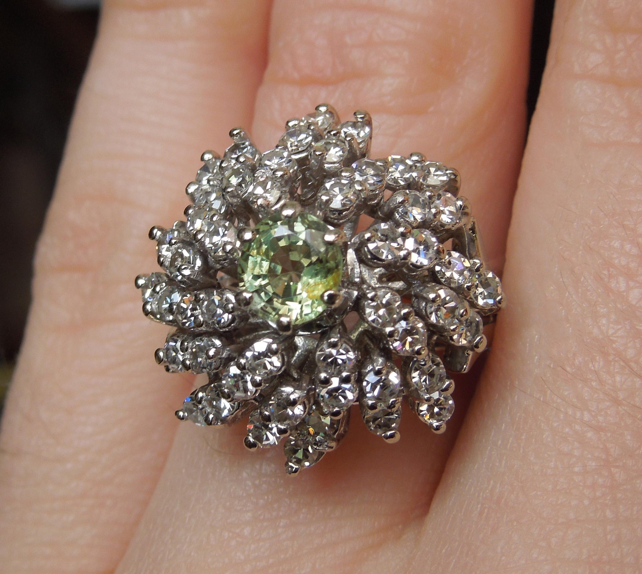 This Mid Century cocktail ring features a central Round cut Natural Light Chameleon Green Alexandrite weighing approximately 0.90 carats measuring 6mm in diameter secured in six prongs, surrounded by 48 Colorless Nearly Flawless Single cut Diamonds