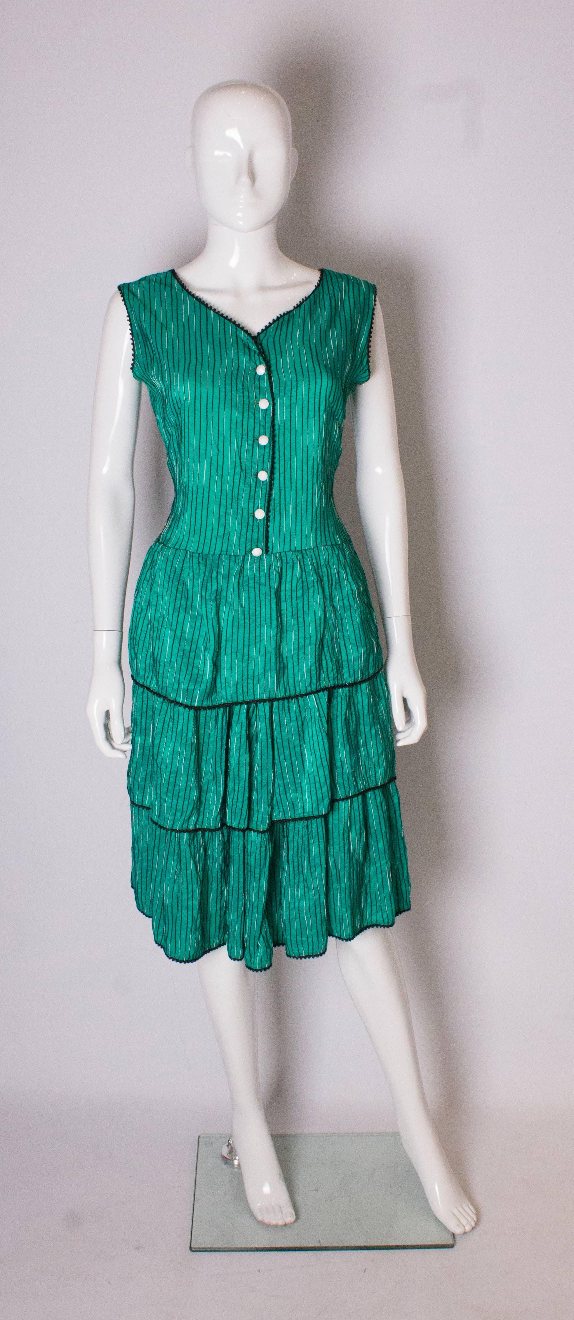 A great vintage sundress in a bright emerald green fabric with black and white stripes, and white buttons down the front.  It has a drop waist, 2 layers of ruffles, and black braid along the neckline and armholes.