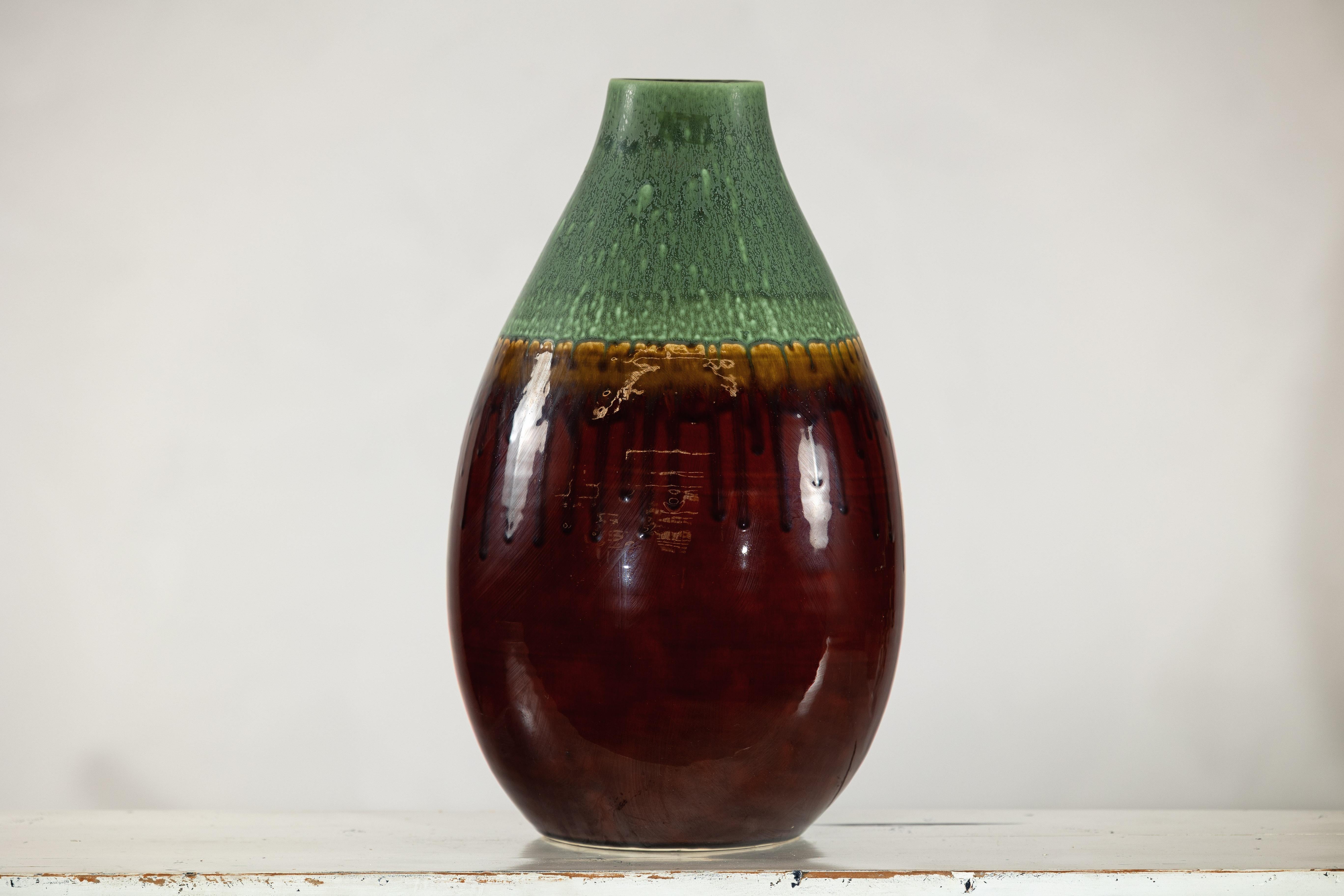 Vaso in ceramica smaltata con la parte centrale arrotondata e una ricca smaltatura bicolore, che mescola il marrone intenso con un fluente effetto a goccia verde. La transizione organica tra i colori crea un'estetica naturale e terrena, esaltata