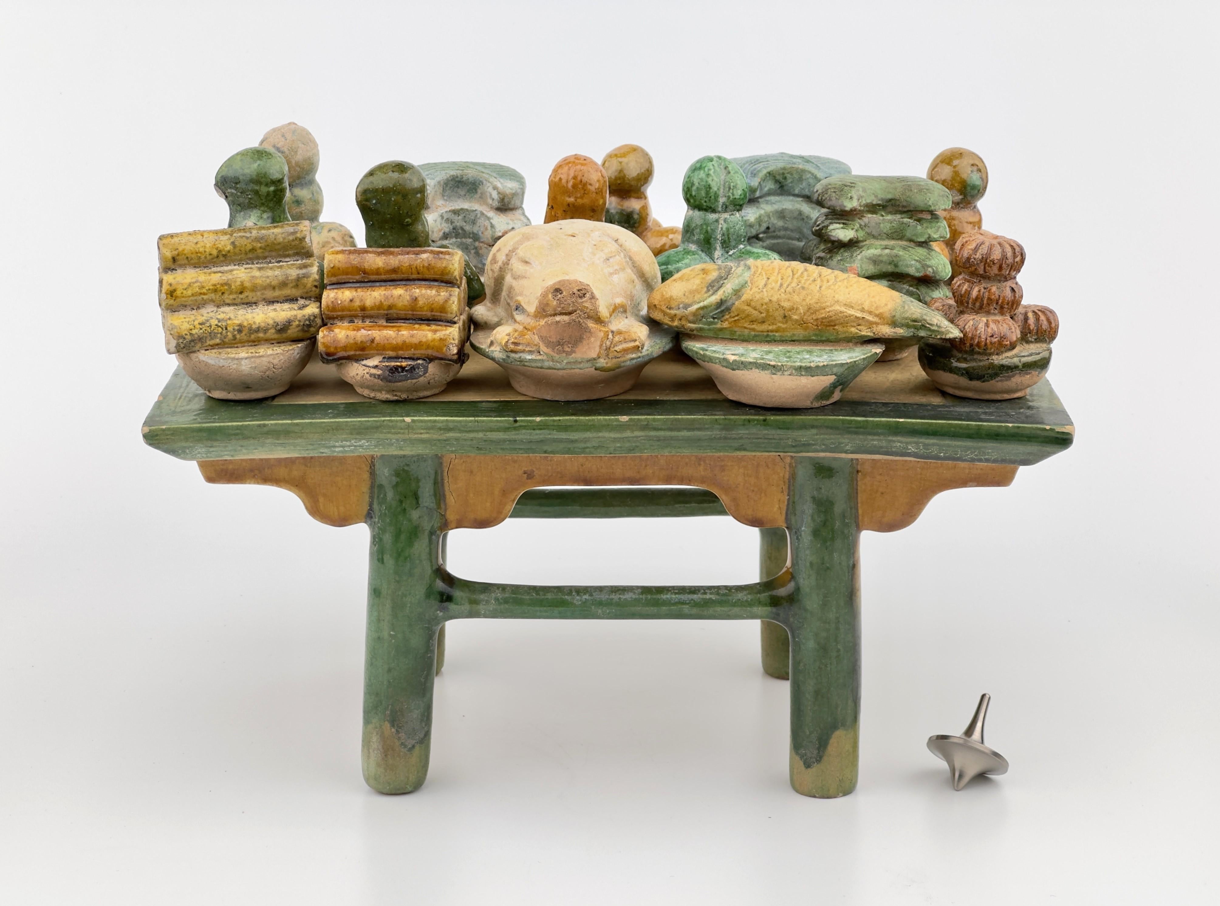 The table bearing pig head, rice cakes, dishes of meat, fish and fruit. Known as Mingqi, these terracotta models were customarily included in Chinese burial practices, particularly among the affluent, to aid the deceased in their journey through the