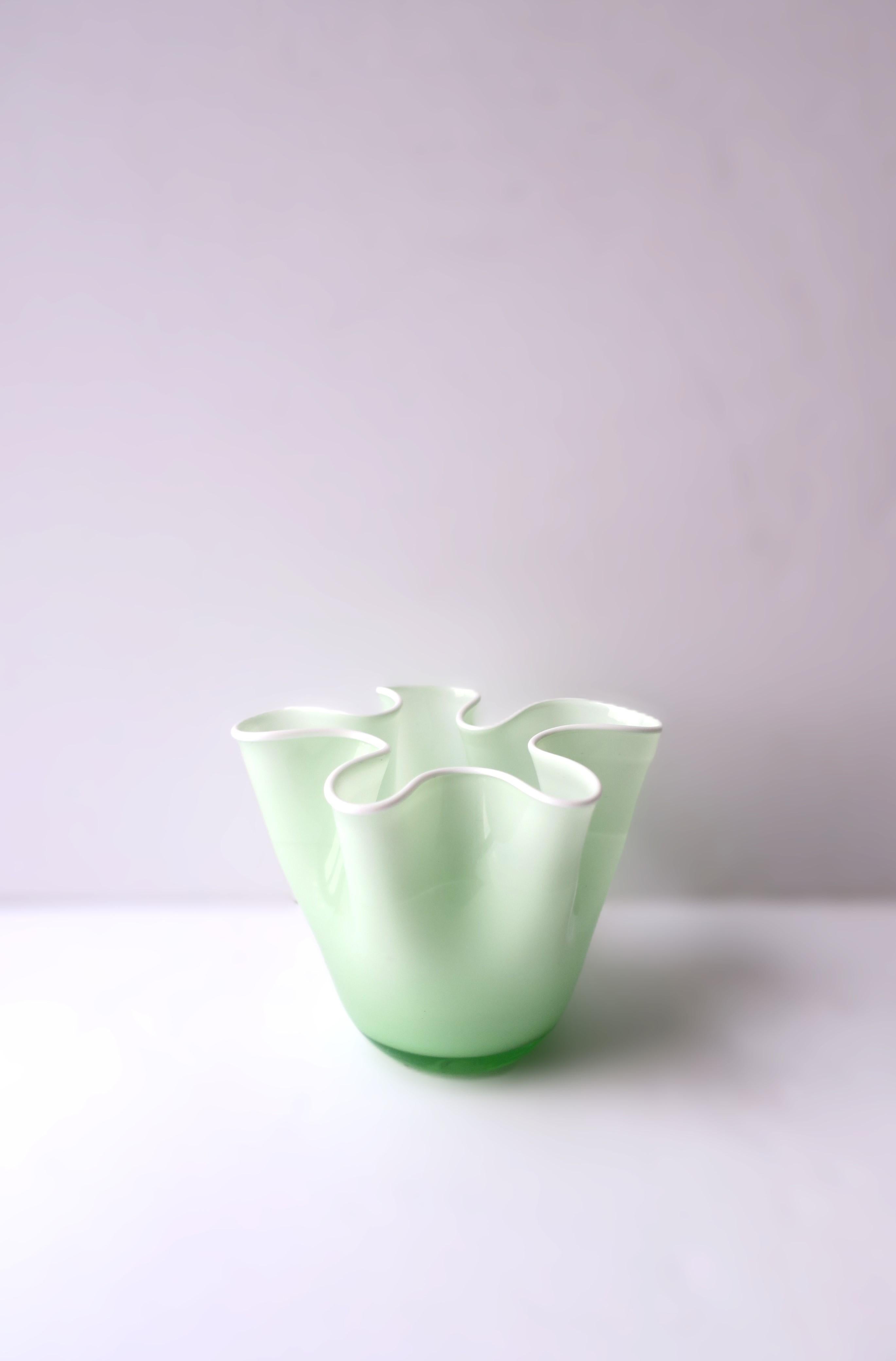 Un vaso in vetro artistico verde e bianco a forma di fazzoletto. Il vaso è stato realizzato a mano, da qui il segno di soffiatura a mano sul lato inferiore, come mostrato nell'ultima immagine. Il vaso è bianco all'interno e verde chiaro all'esterno,