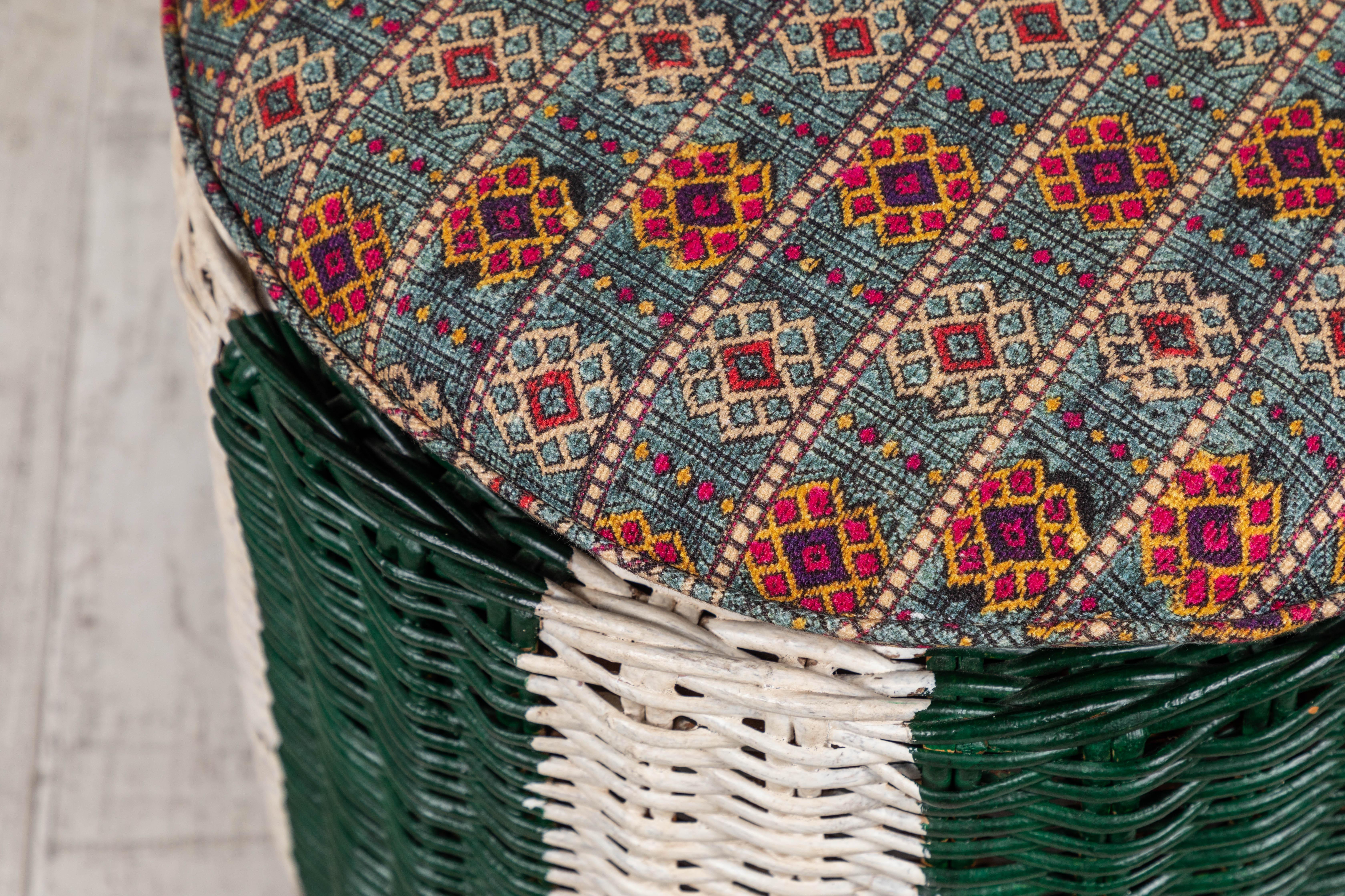 Round green and white painted wicker ottoman with colorful pillow topped cushion.