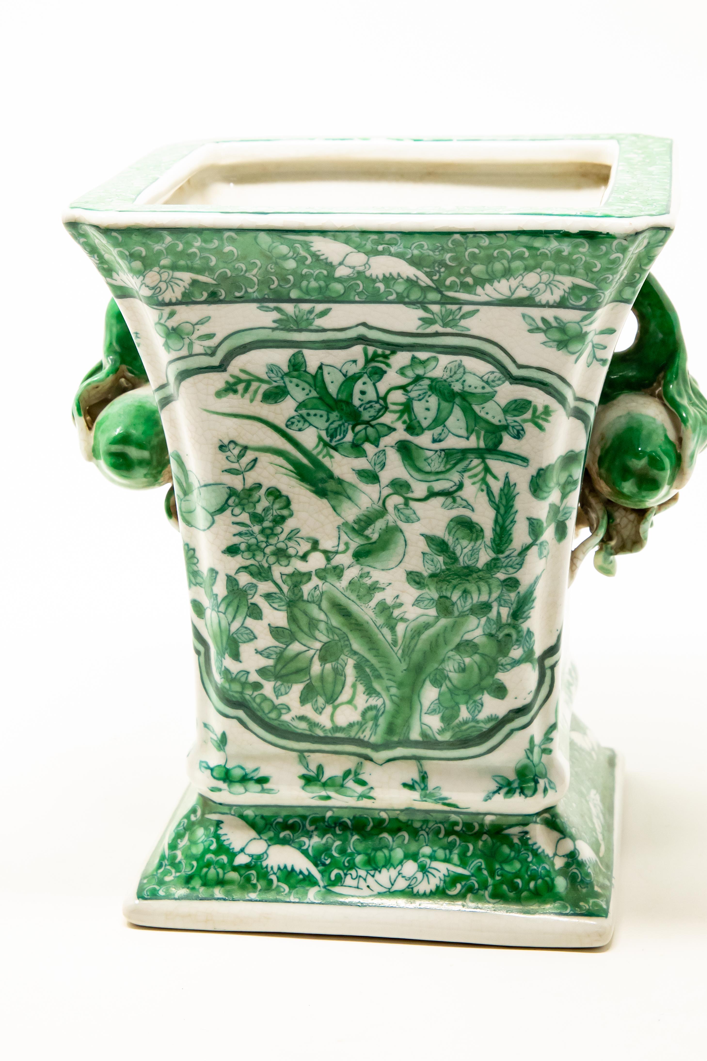 Offering this green and white vase. Hand painted in green with floral and foliate detail. The vase is square in shape and has two handles that are fruit themed.
