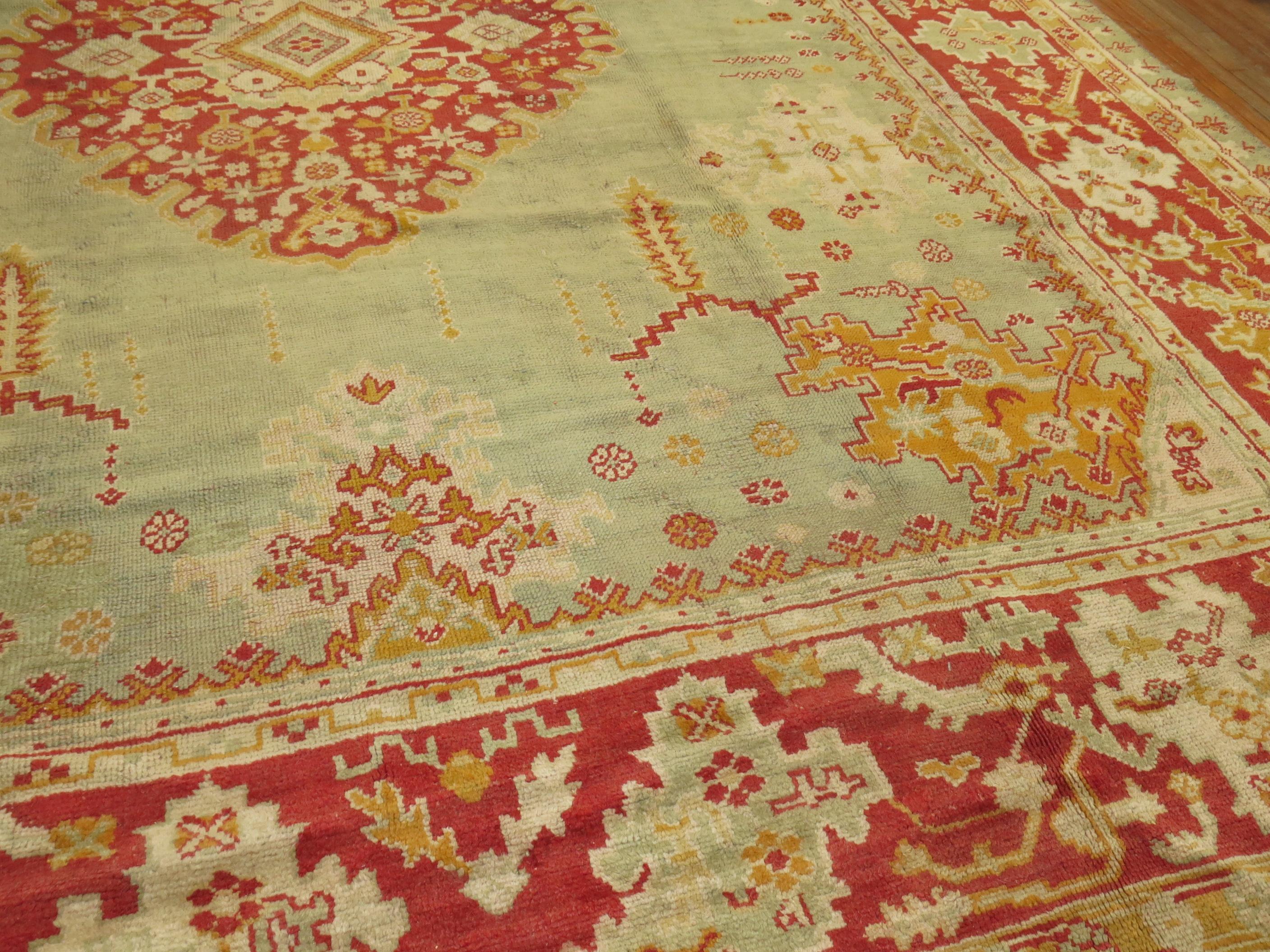 A large square early 20th-century antique Turkish Oushak rug with a light green field and red border. Full pile condition. 

Measures: 13'8” x 15'3”

Oushak rugs originated in the small town of Oushak in west-central Anatolia, today just south of