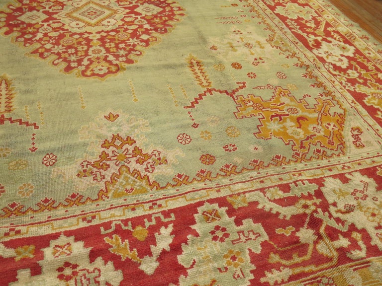 A large square early 20th century antique Turkish Oushak rug with a light green field and red border. Full pile condition. Measures: 13'8” x 15'3”

Oushak rugs originated in the small town of Oushak in west-central Anatolia, today just south of