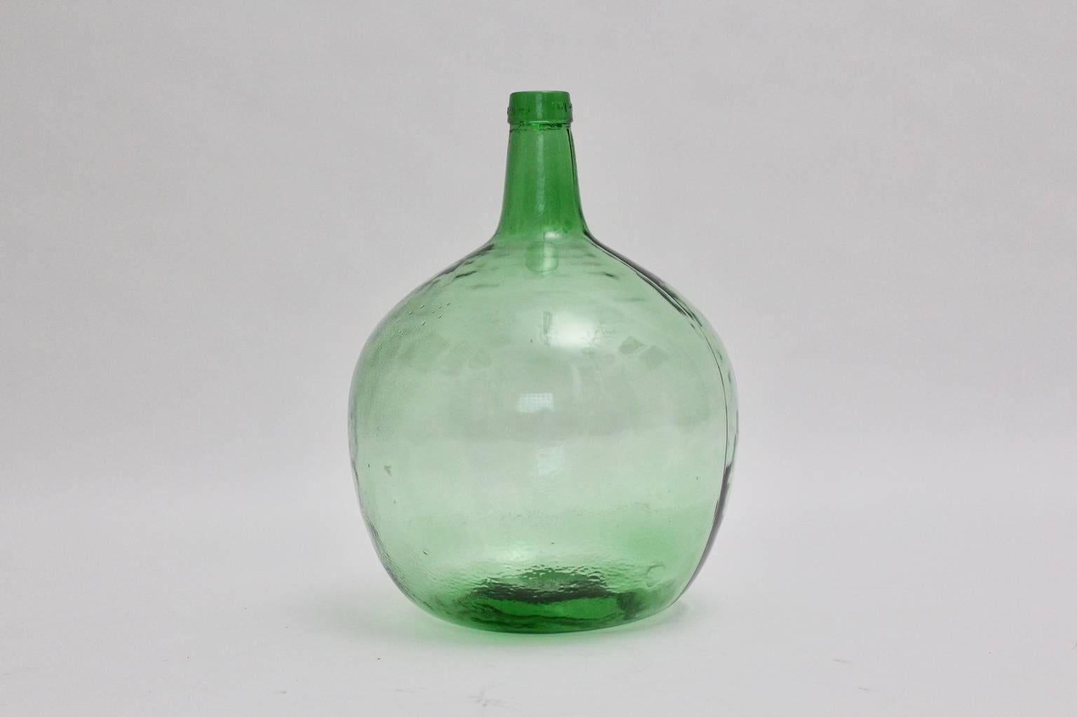 Green vessel or Demijohn by Viresa, 1970s, which is very decorating and would work perfect as a flower vessel.
Throughout the beautiful emerald bright green color tone and the round shape the green vintage glass vessel would be an amazing detail in