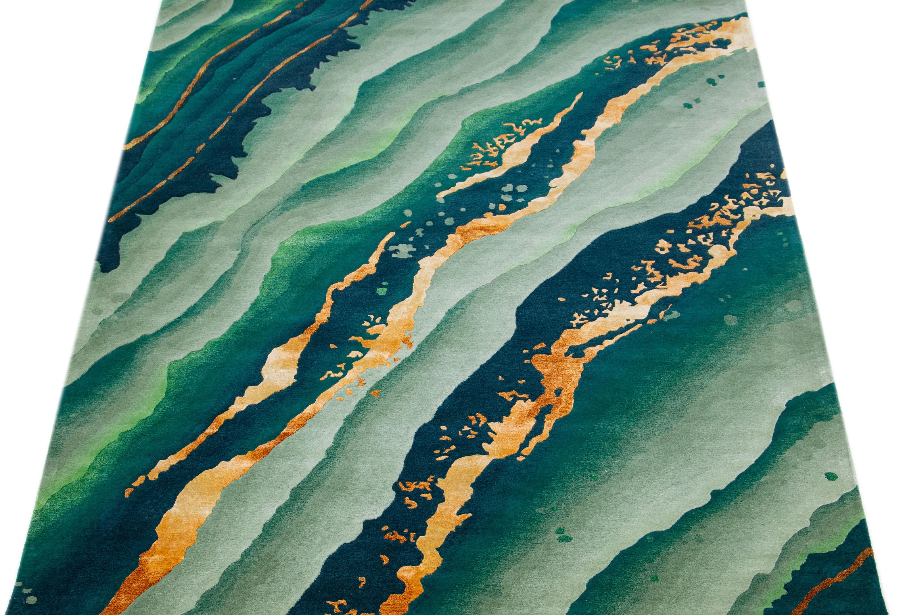 Dieser moderne Wollteppich zeigt ein abstraktes grünes Feld mit dekorativen goldenen Akzenten. Das All-Over-Design verkörpert den Geist des Modernismus im 21. Jahrhundert und macht ihn zu einer wirklich raffinierten und modischen Ergänzung für jede