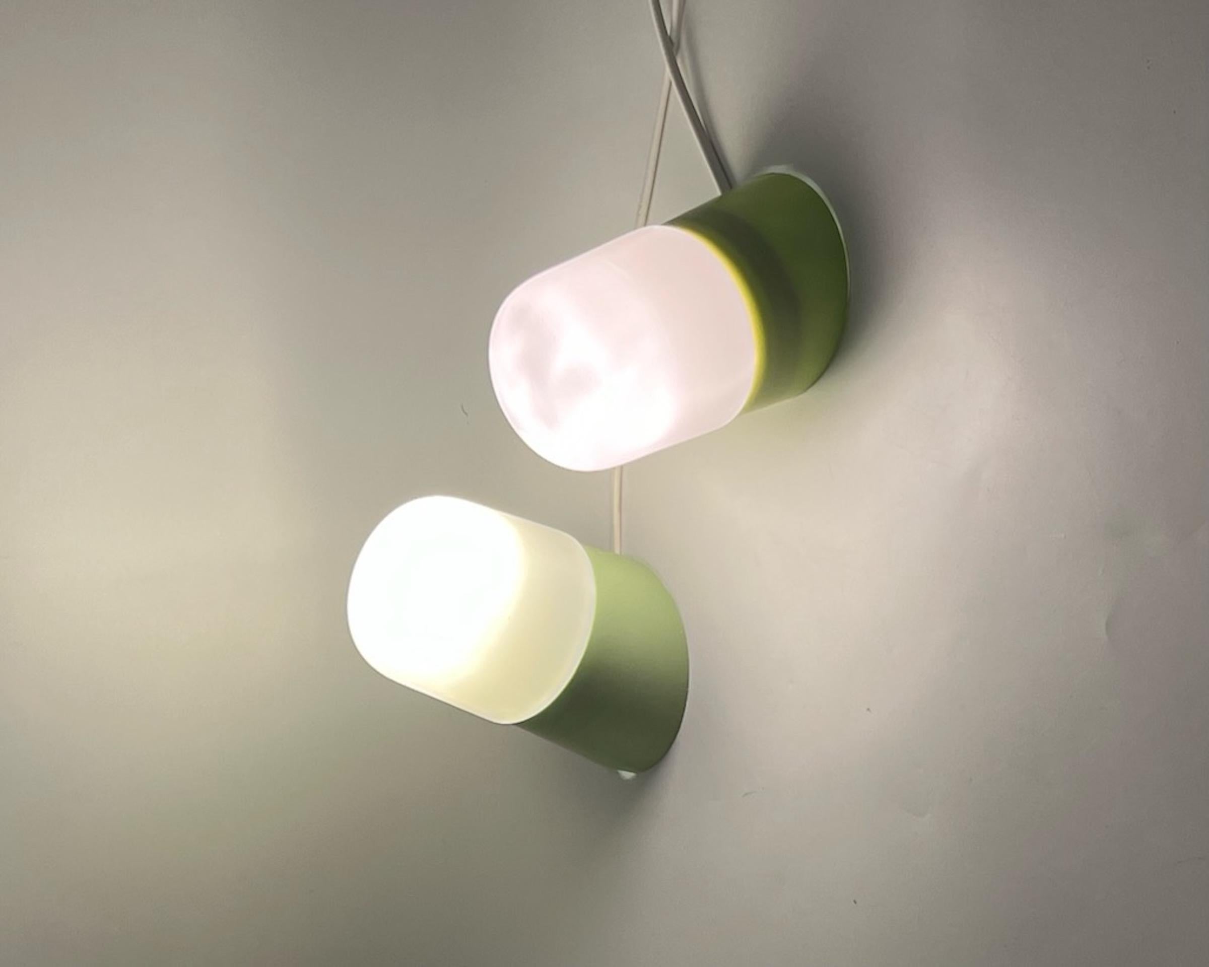 Jolie série d'appliques vertes en forme de pilule datant des années 60. Ces charmantes lampes au design industriel sont composées d'une base en bakélite. L'abat-jour est en verre opalin épais et la douille est en céramique authentique.

Cette lampe