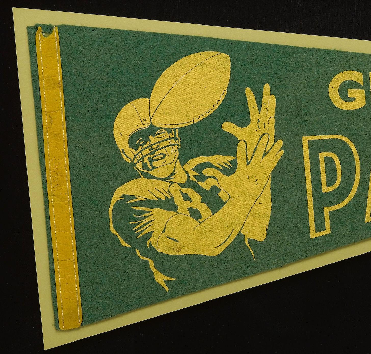 Presented is a vintage green bay packers felt pennant from 1967. The pennant is composed of green felt, with yellow printed lettering, and a yellow felt headband, stitched on in a running stitch. The pennant has yellow block lettering that reads