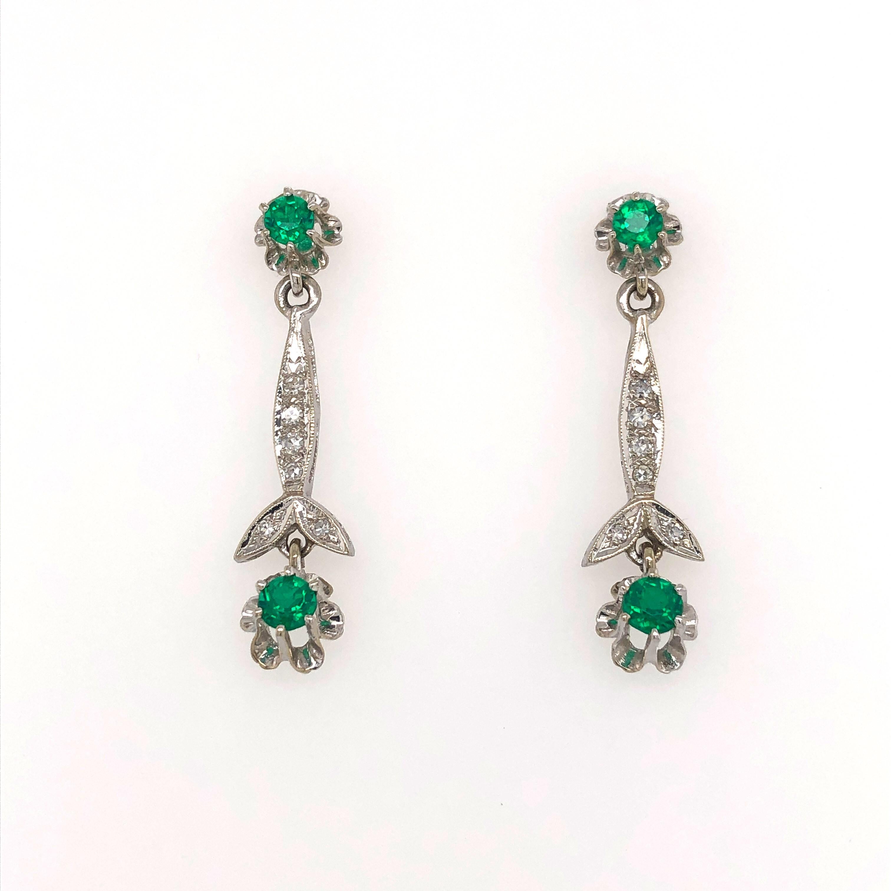 Flirty drop earrings of fourteen carat white gold with diamond accented floral stems display vivid green beryl floral buds and studs. The four beryl doublet stones of .06 ct each are prong set giving dimension to the design. The drop is 1-1/4 inches