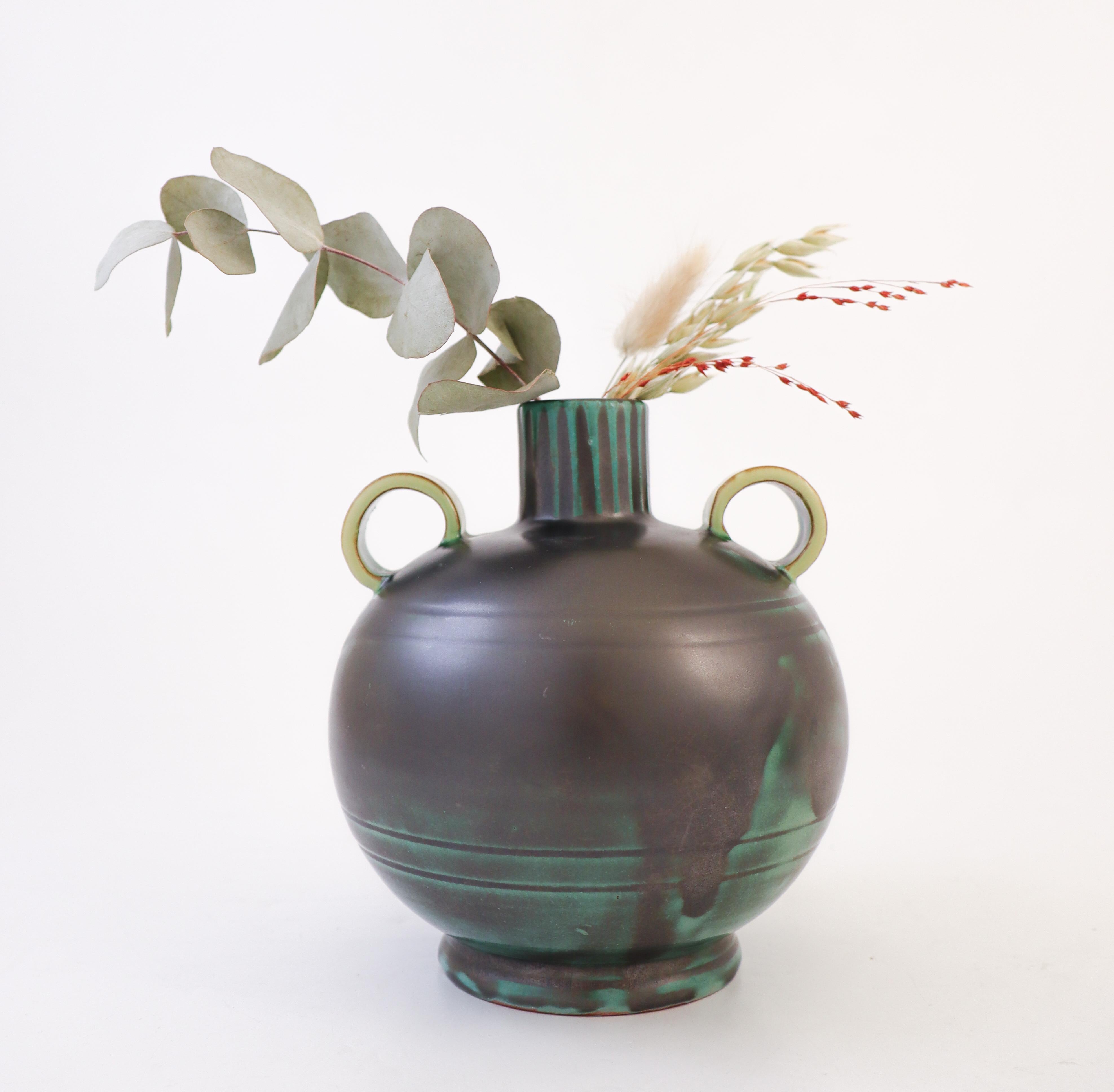 Precioso jarrón de cerámica negra y verde con asas amarillas y forma clásica Art Déco, diseñado en Upsala Ekeby entre 1932 y 1938. Mide 16 cm de alto y unos 14 cm de diámetro y está en excelente estado. Tiene una marca impresa con 2646 y Upsala