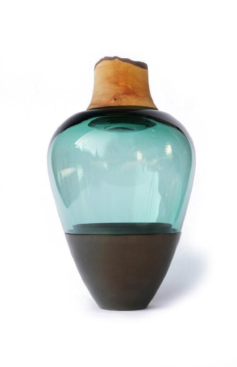 Green blue and brass Patina India Vessel I, Pia Wüstenberg.
Dimensions: D 20 x H 38.
Materials: glass, wood, brass.
Available in other metal: copper, brass patina.

Handmade in Europe, by individual craftsmen: handblown glass (Czech Republic),