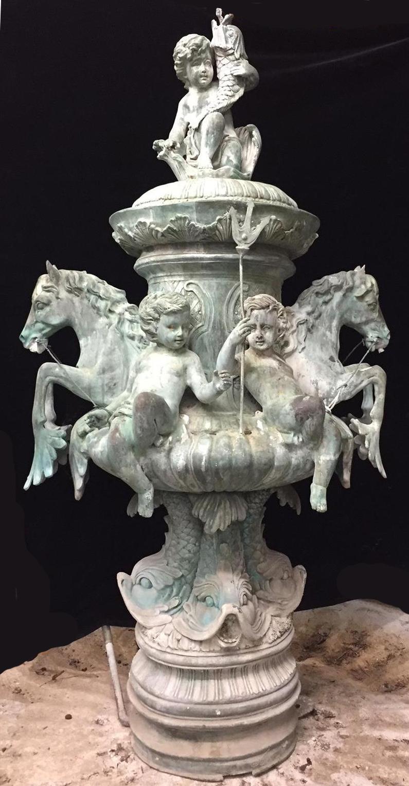 Impressive continental weathered green patinated bronze figural fountain.

A single cherub sitting on a shell form sleigh holding a fish in one hand. Two pairs of sitting cherubs with a rope holding two horses on either side of them, supported by