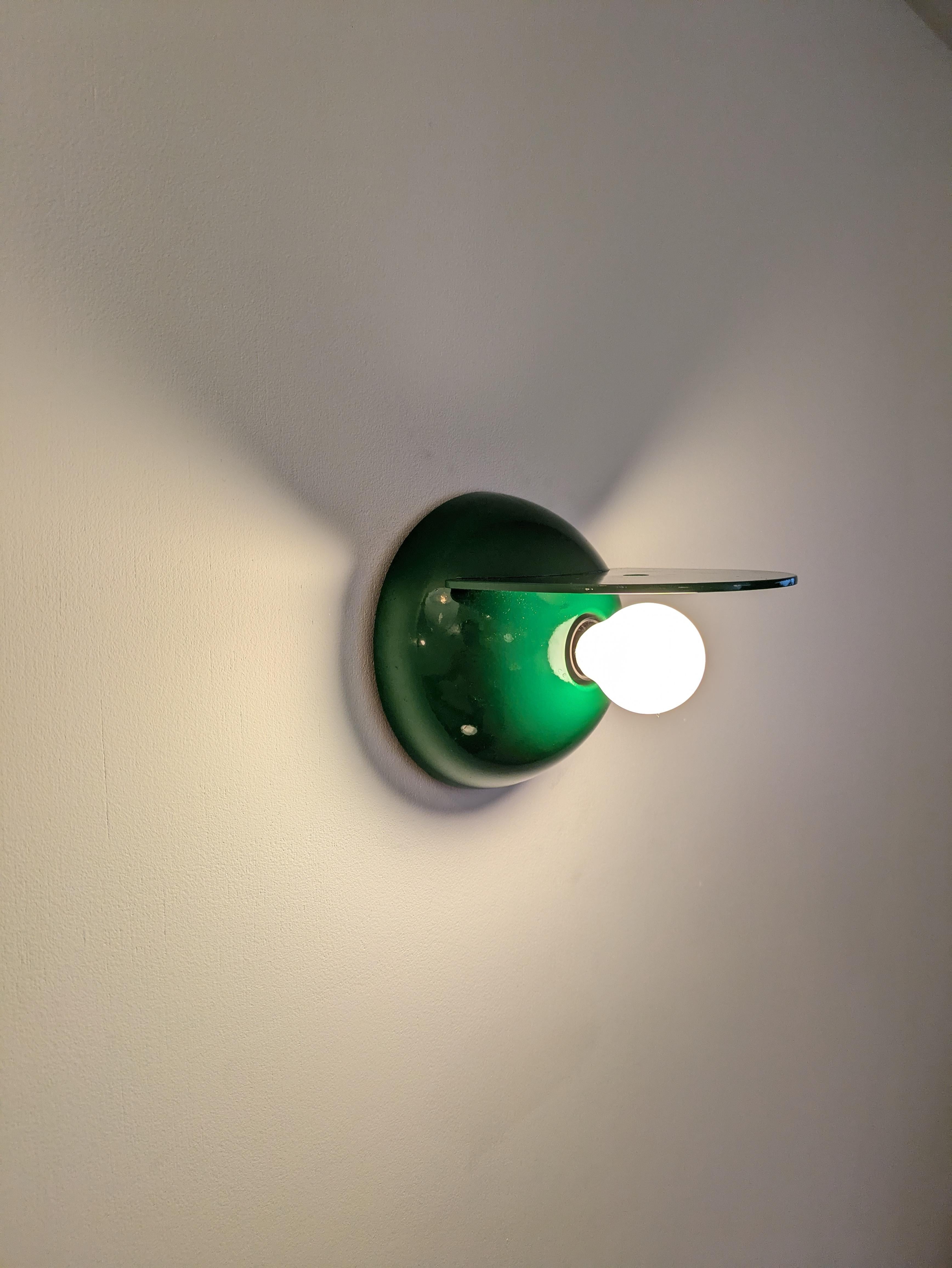 Este aplique Buco (Agujero) es de fabricación italiana y está fabricado por Artemide. Fue diseñada por el diseñador italiano Claudio Dini. 
Está hecha de plástico 💚 verde (ABS) sobre un soporte de plástico negro que permite que la parte verde