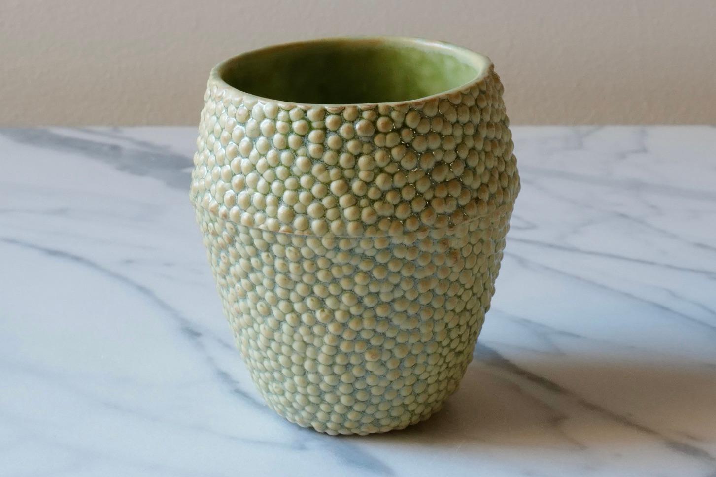 Elegant ceramic drinking cup. Hand-cast in porcelain using a mold hand-carved by the artist. The glaze is an earthy green color that highlights the delicate texture by deepening in color around each spherical form. The ‘caviar’ texture is evocative