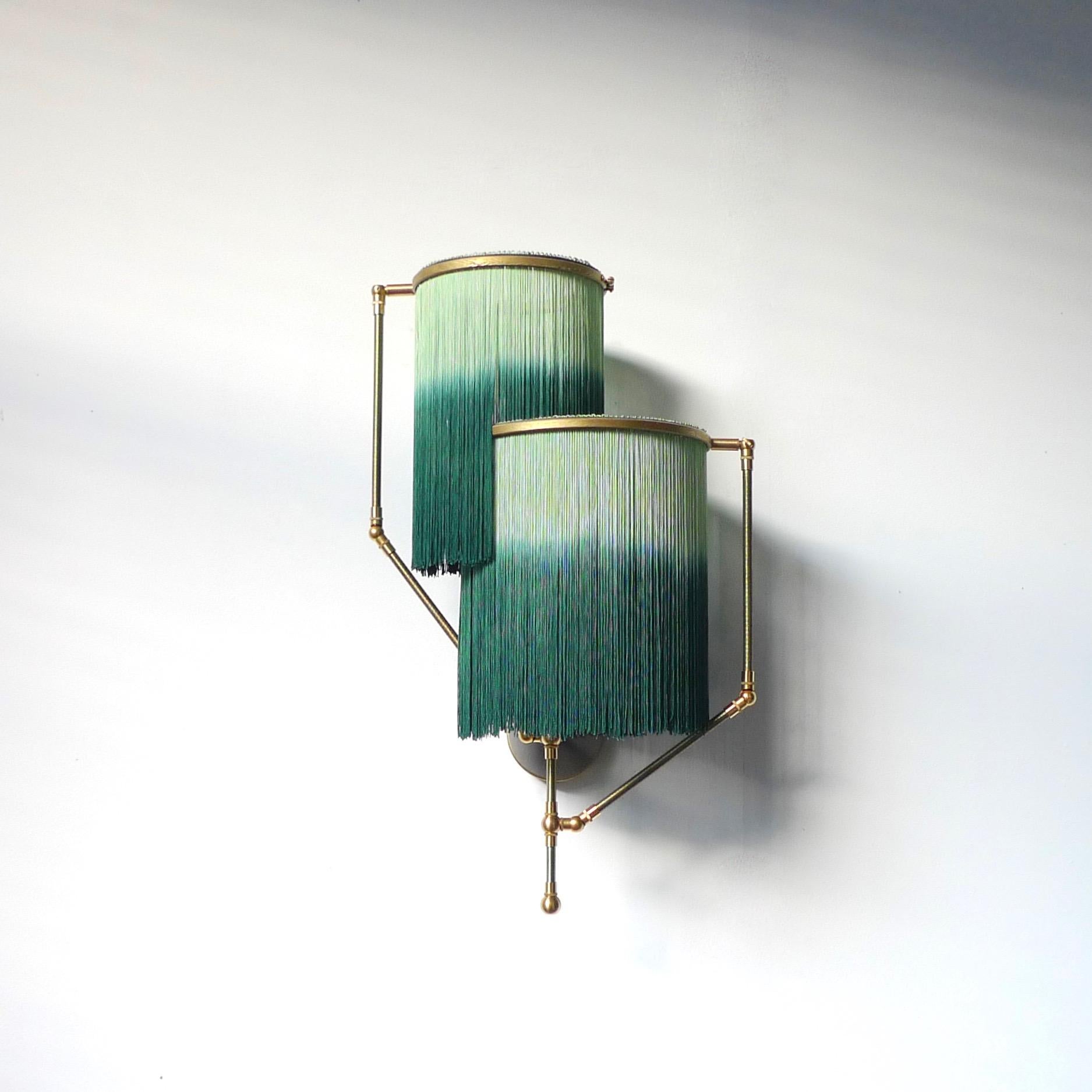Lámpara aplique charme verde, Sander Bottinga.

Dimensiones: 50 x A 38 x P 27 cm.
Hecho a mano en latón, cuero, madera y flecos de colores teñidos por inmersión en viscosa.
Los brazos móviles permiten colocar los círculos con franjas en