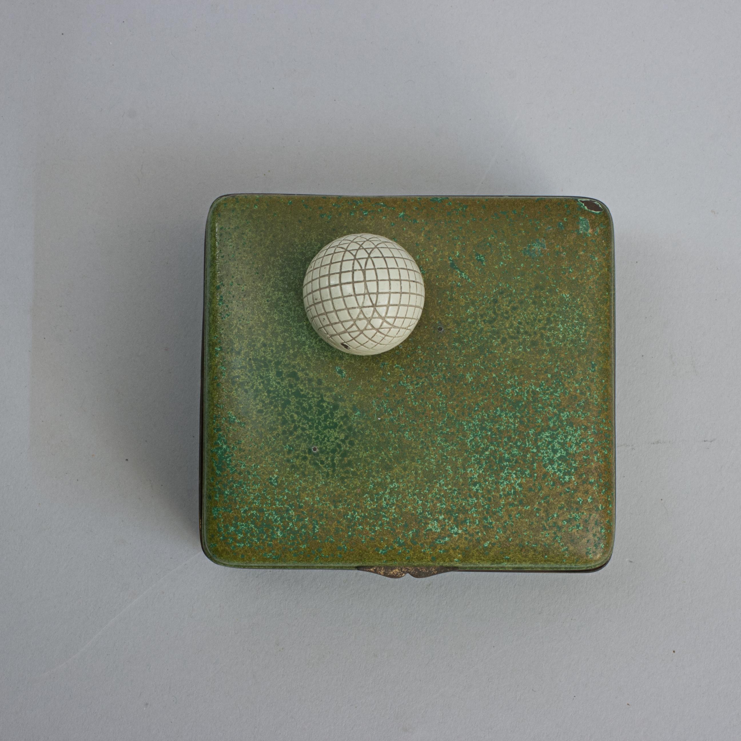 Caja de golf de hojalata verde.
Pequeña lata de cigarrillos de golf con el interior forrado de madera de cedro, acabado con textura de hierba verde, rematada con un modelo de pelota de golf de tripa de malla. Originalmente era un artículo para