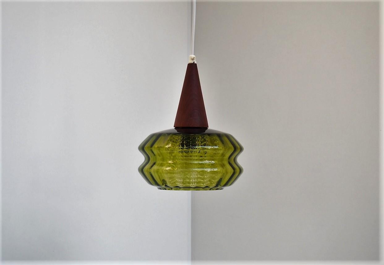 Beautiful shaped green crystal pendant with a teak top and an inner shade made in clear crystal. The pendant is Swedish design from Carl Fagerlund for Orrefors in the 1960s. 

The shine from the pendant is very special because of the shape but